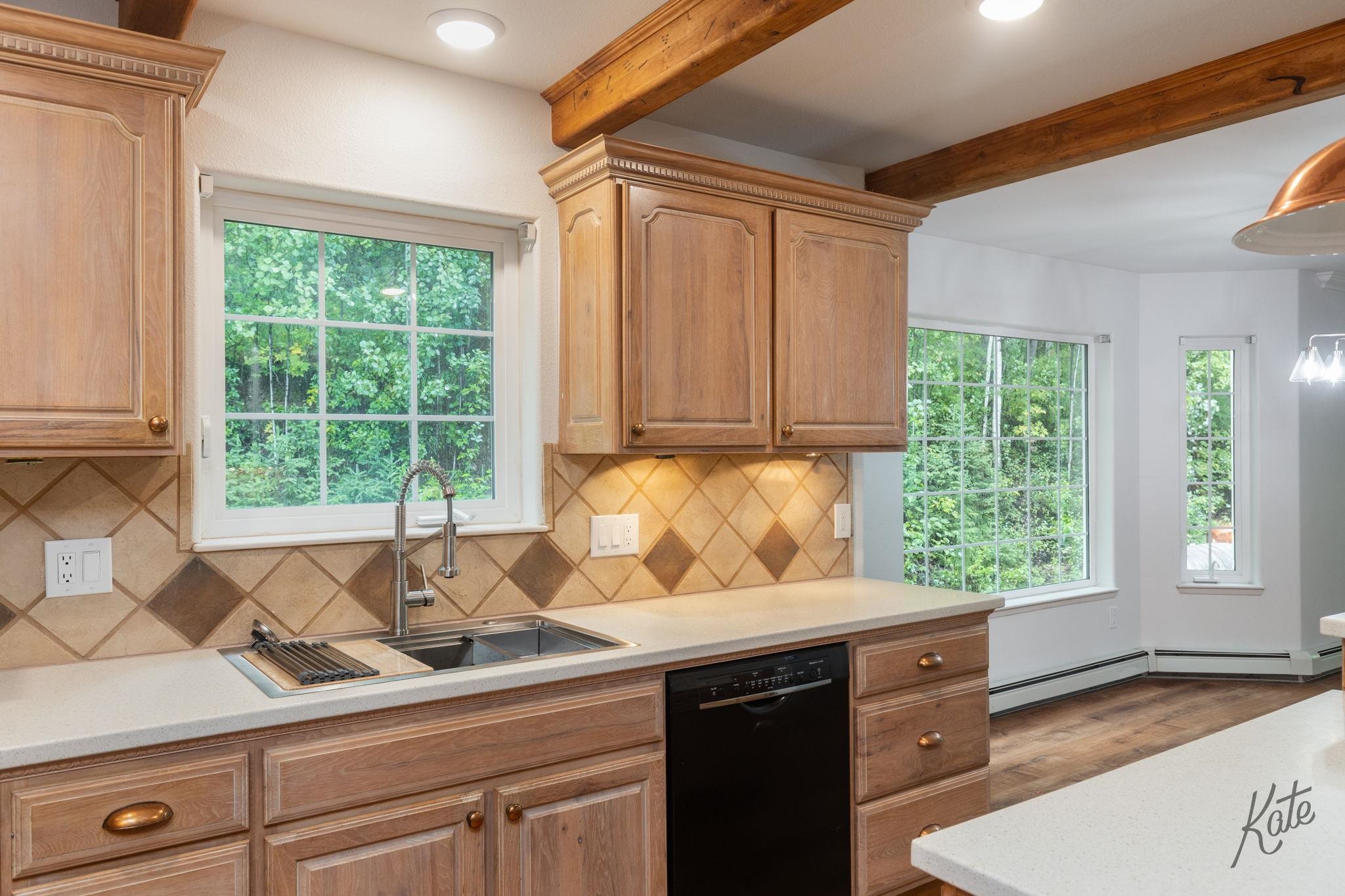 Kitchen with wood cabinets, diamond-pattern tile backsplash, and large windows overlooking trees.