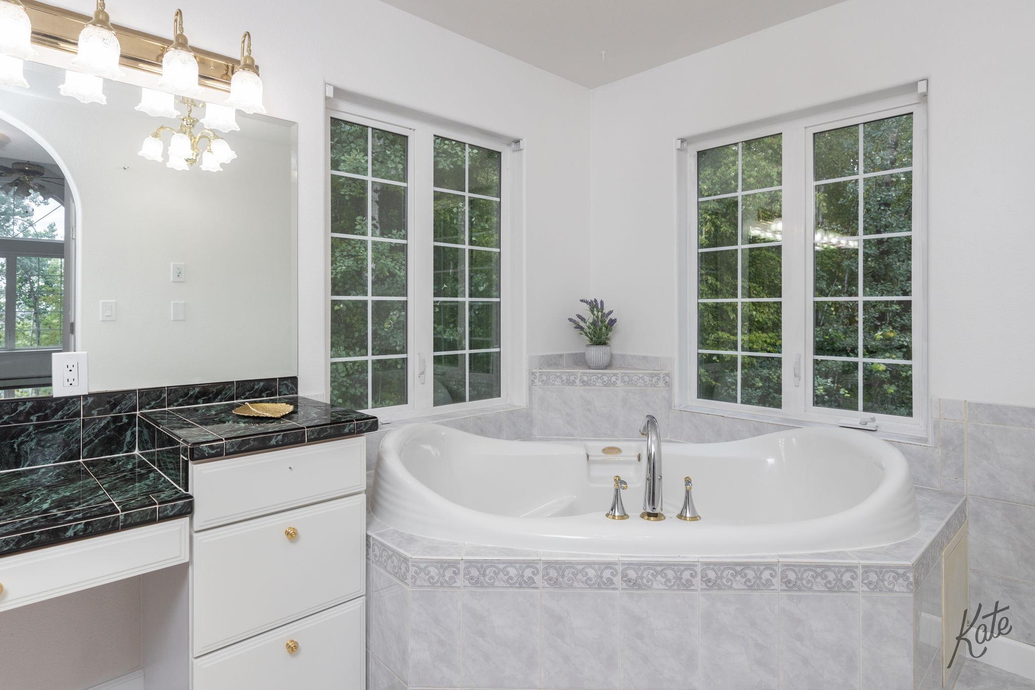 Bathroom with a large corner soaking tub beneath tall windows and a dark marble vanity.