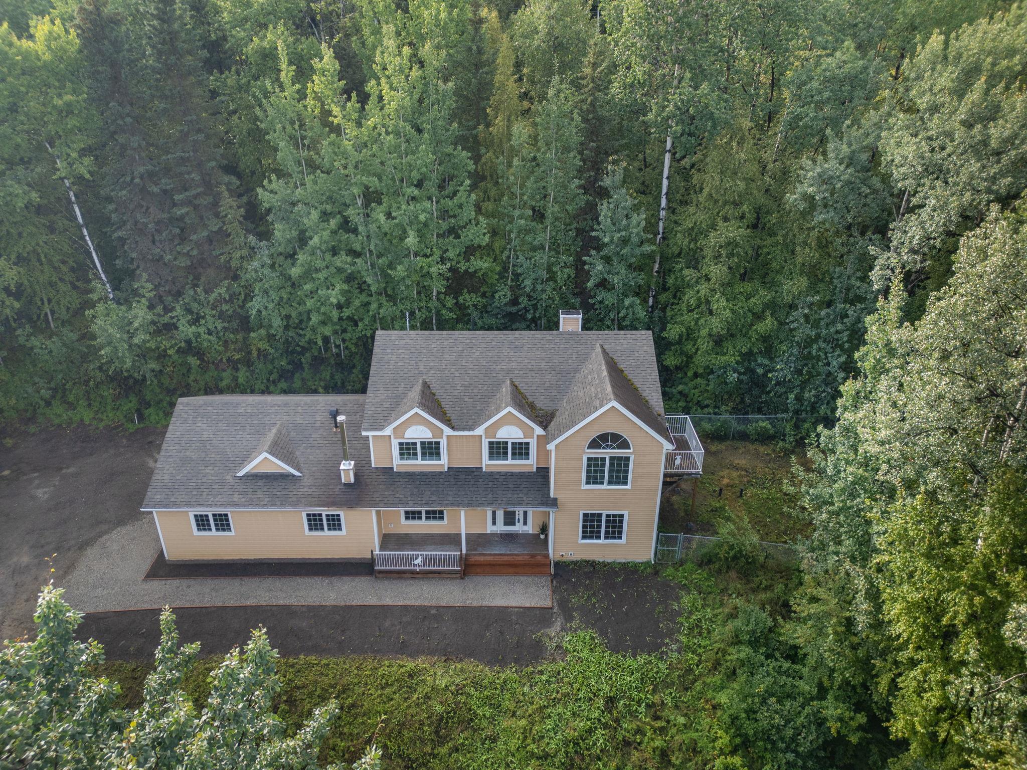 Aerial view of a tan multi-story home with a front porch, surrounded by dense trees.