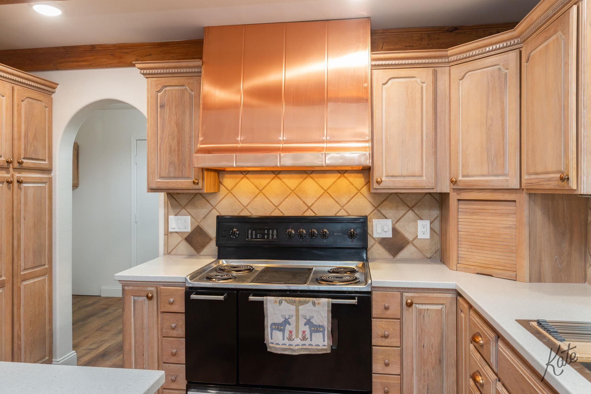 Kitchen with a copper range hood, light wood cabinets, and a black electric range.