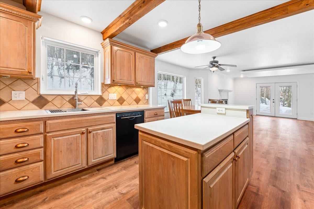 Kitchen with a large wood-paneled island, warm cabinetry, exposed beams, and snowy yard views.