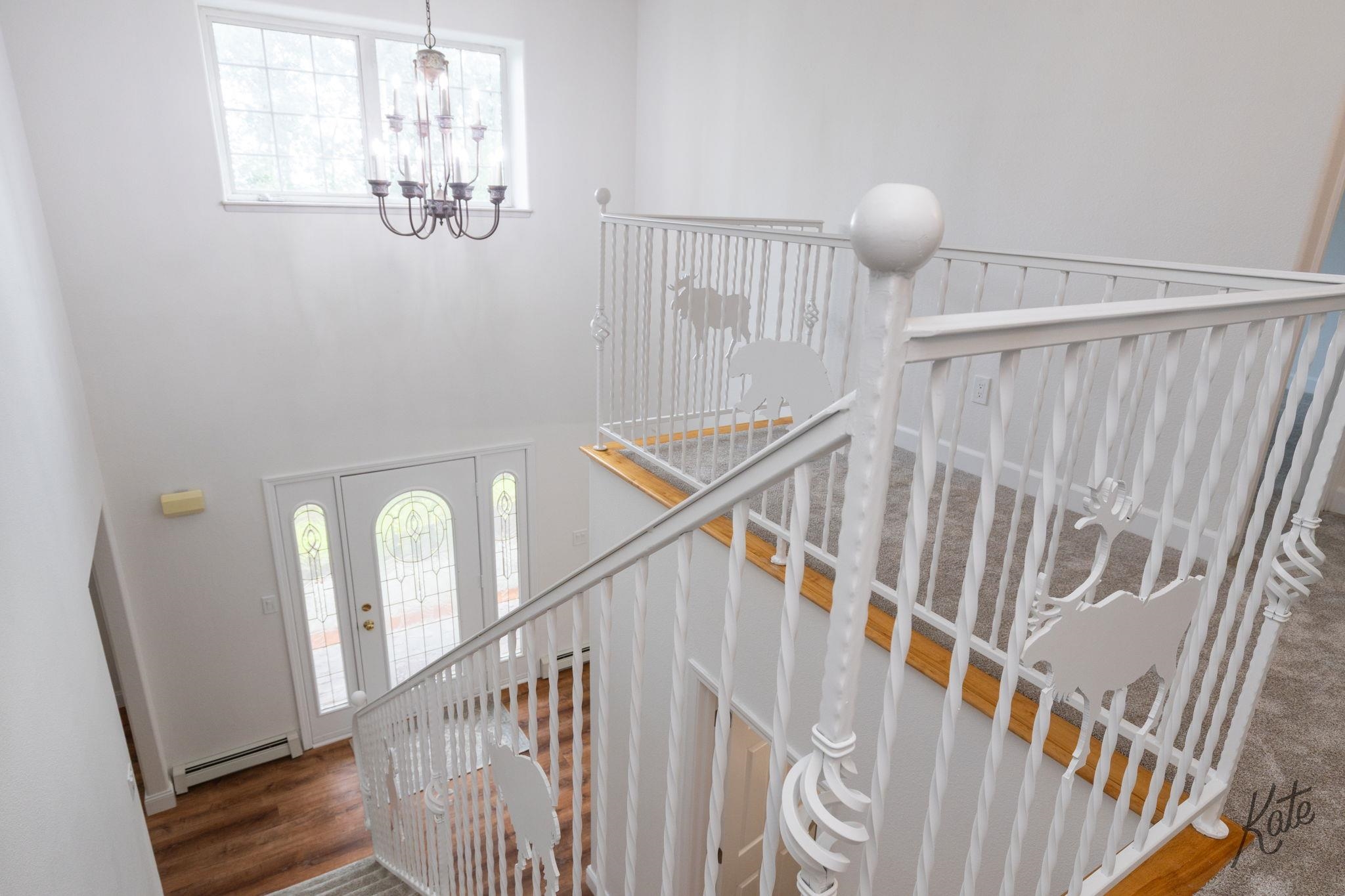 Two-story entryway with white decorative railings, a glass-paneled front door, and a hanging chandelier.