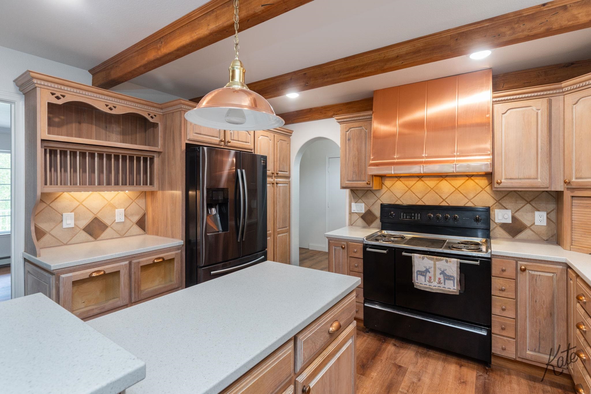 Kitchen with wood cabinetry, exposed beams, a white island, and a copper range hood.
