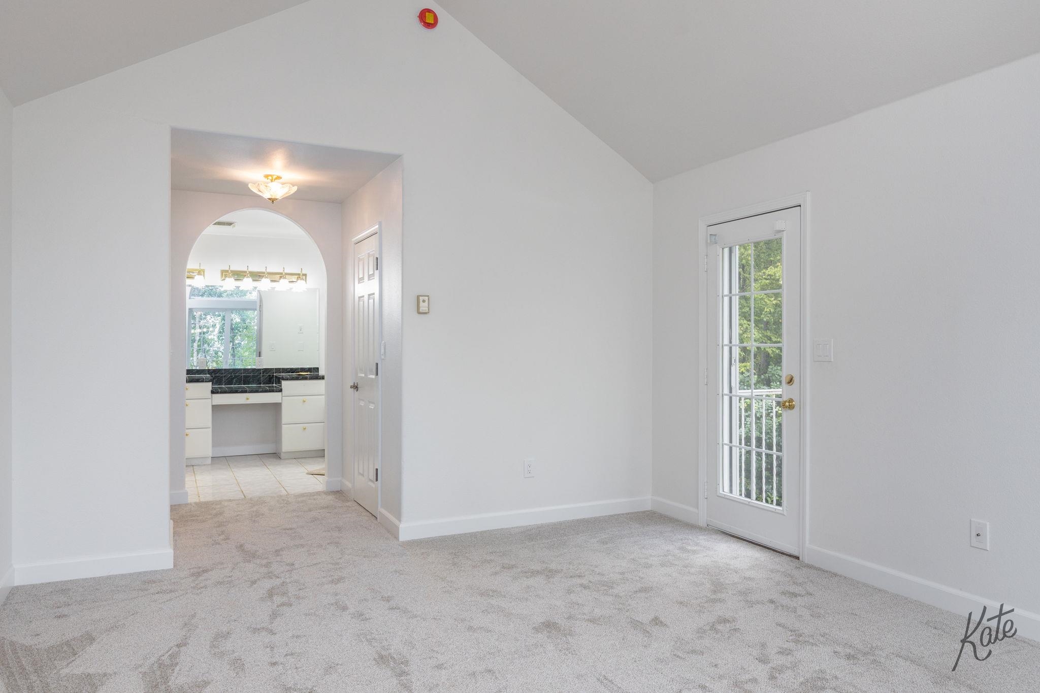 Unfurnished carpeted room with vaulted ceiling, glass-paneled exterior door, and arched opening to a vanity.