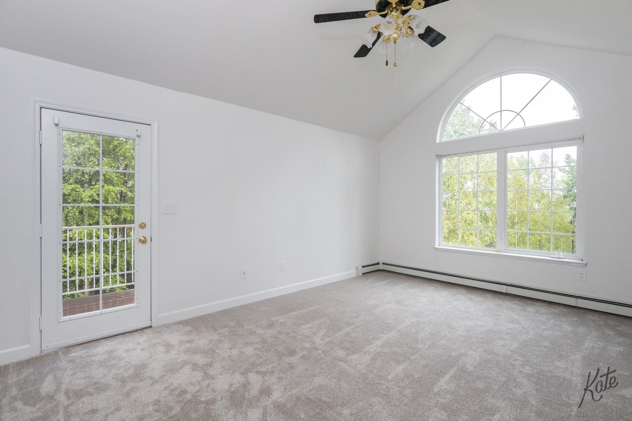 Empty carpeted room with a glass door and large windows beneath an arched window.