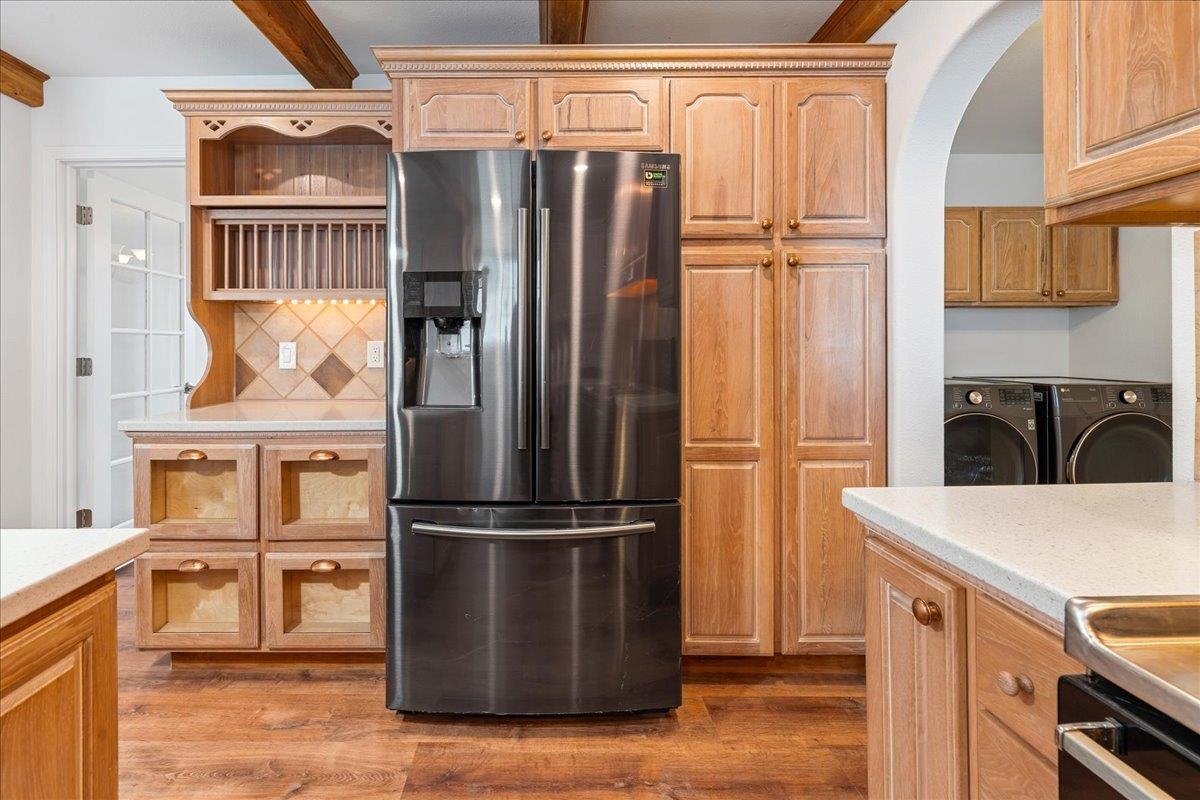 Kitchen with wood cabinetry, a stainless steel refrigerator, and adjoining laundry area.