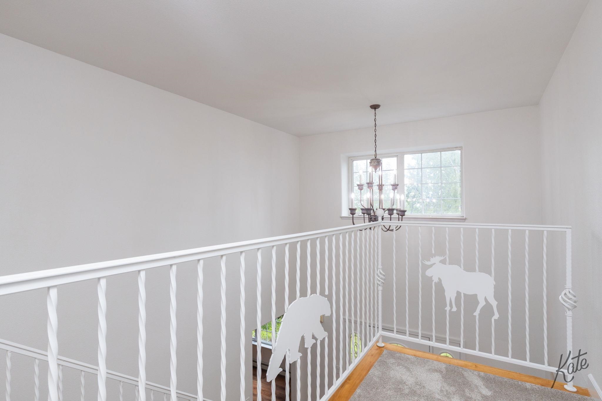 Upstairs landing with white moose-decorated railing, chandelier, and large window.