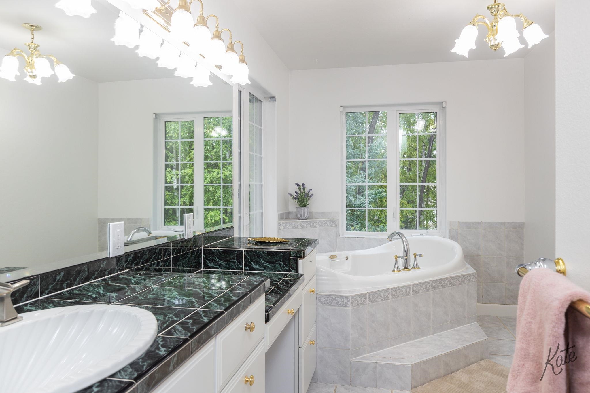 Bathroom with a corner soaking tub, black marble vanity, and windows overlooking trees.
