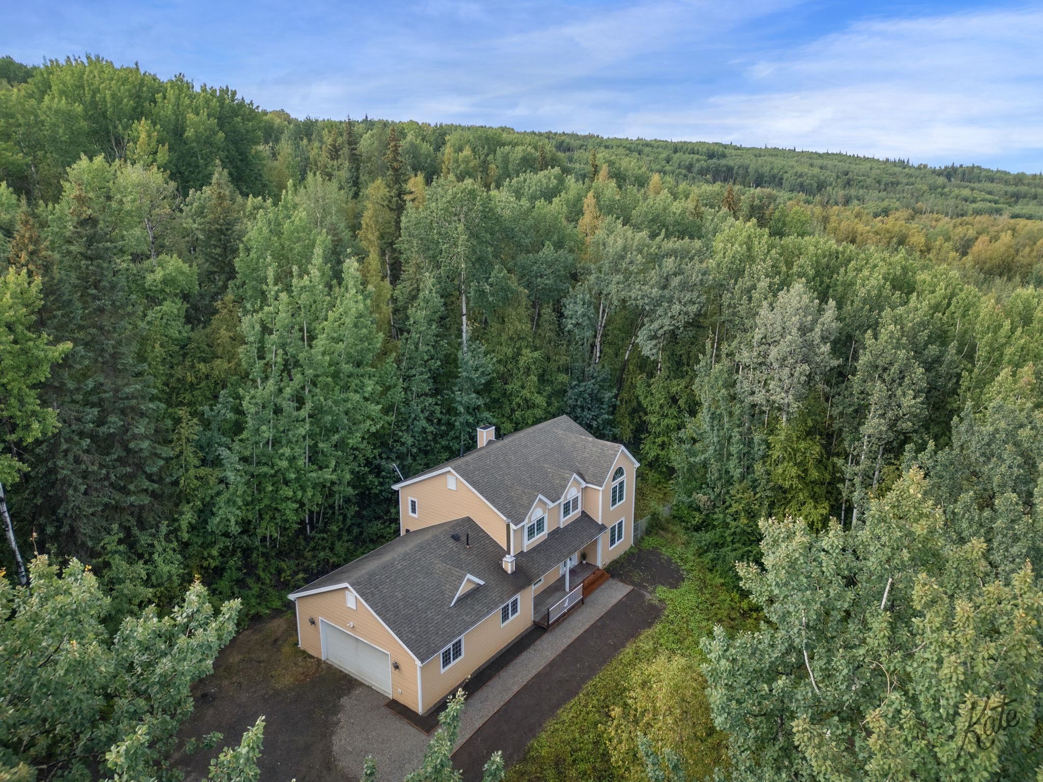 Aerial view of a tan two-story home surrounded by dense forest.