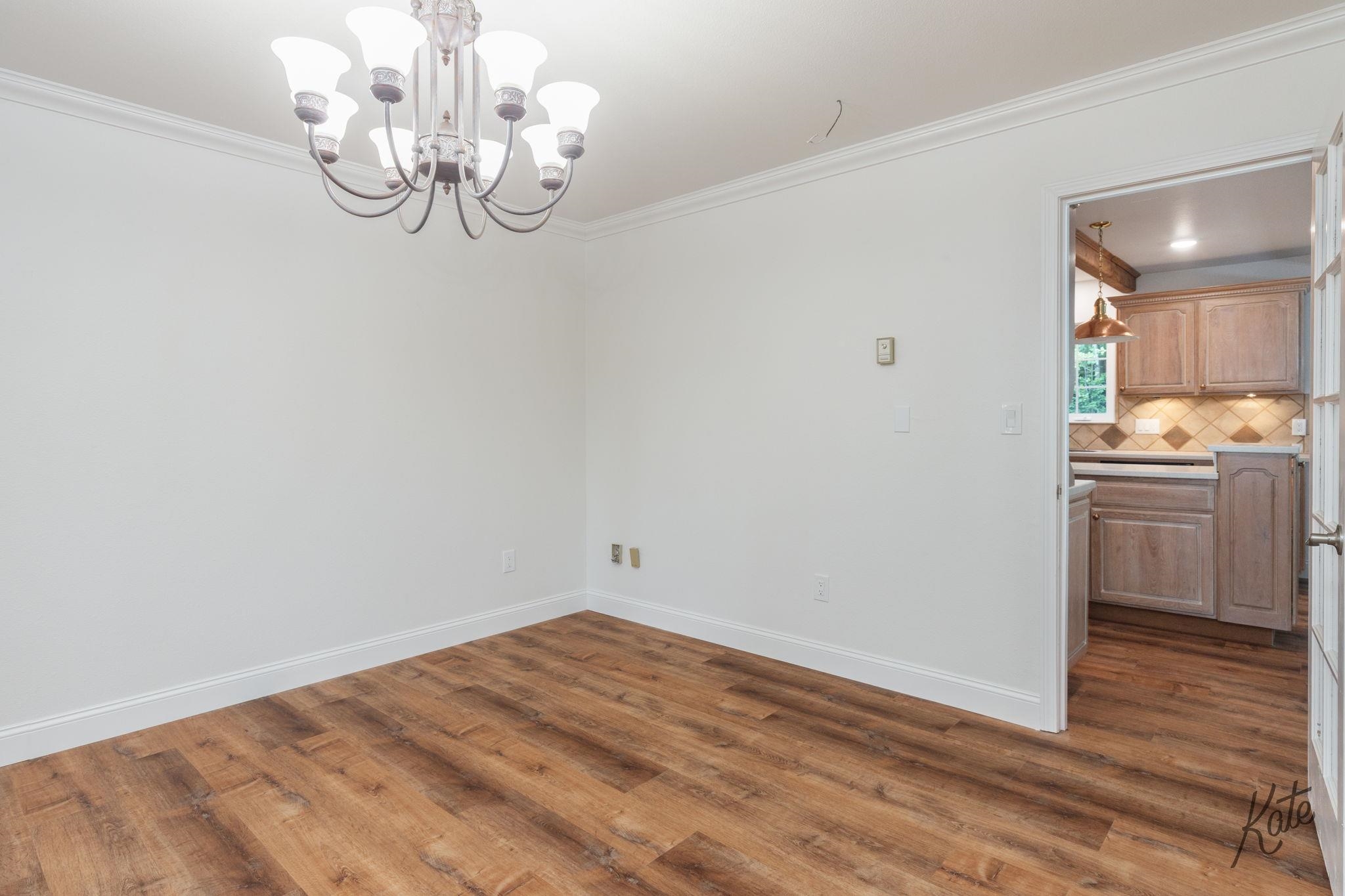 Vacant dining room with wood-look flooring and chandelier, viewed toward the kitchen.