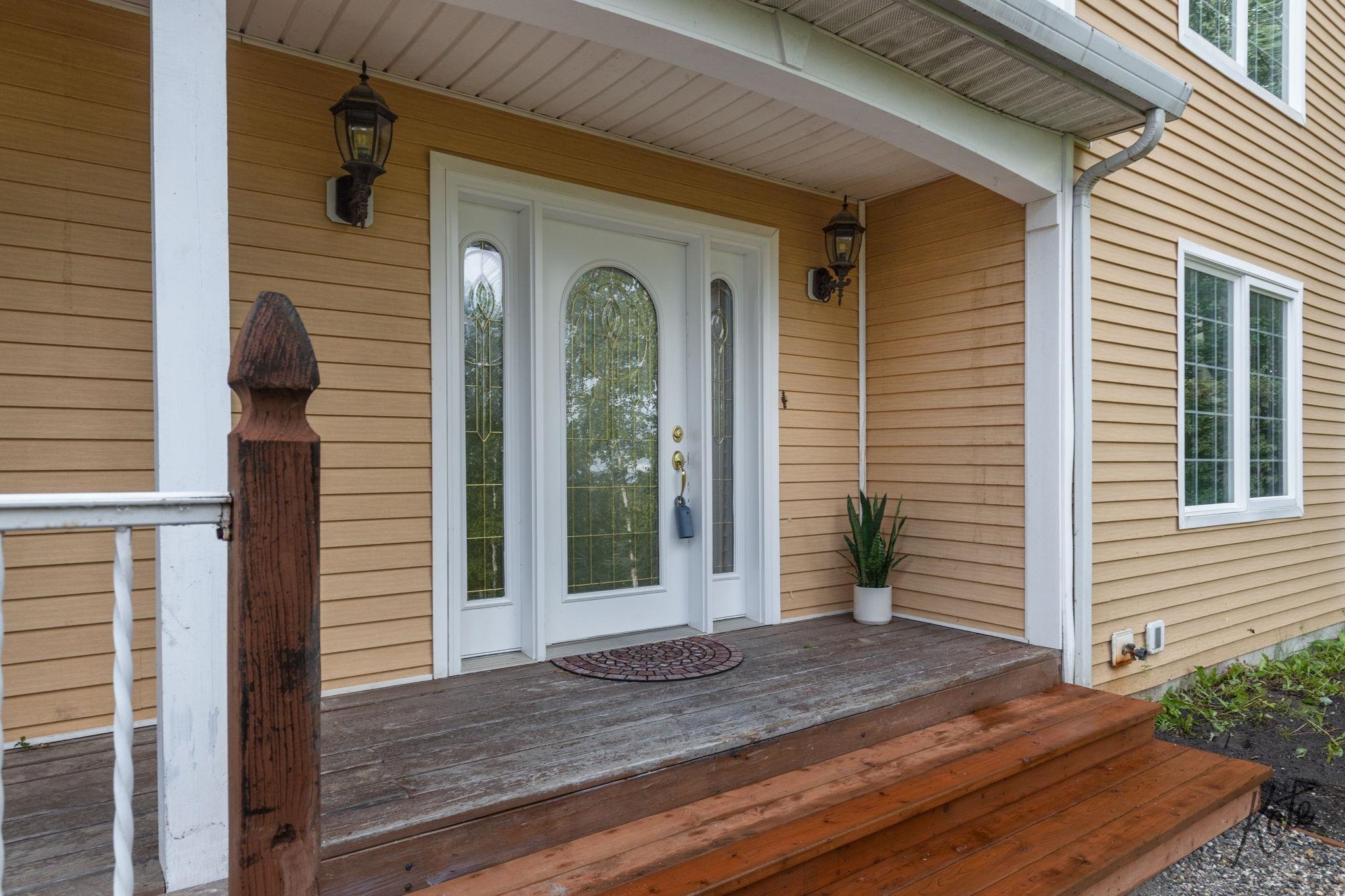 Covered front porch with a white glass-paneled door, lanterns, and wooden steps.