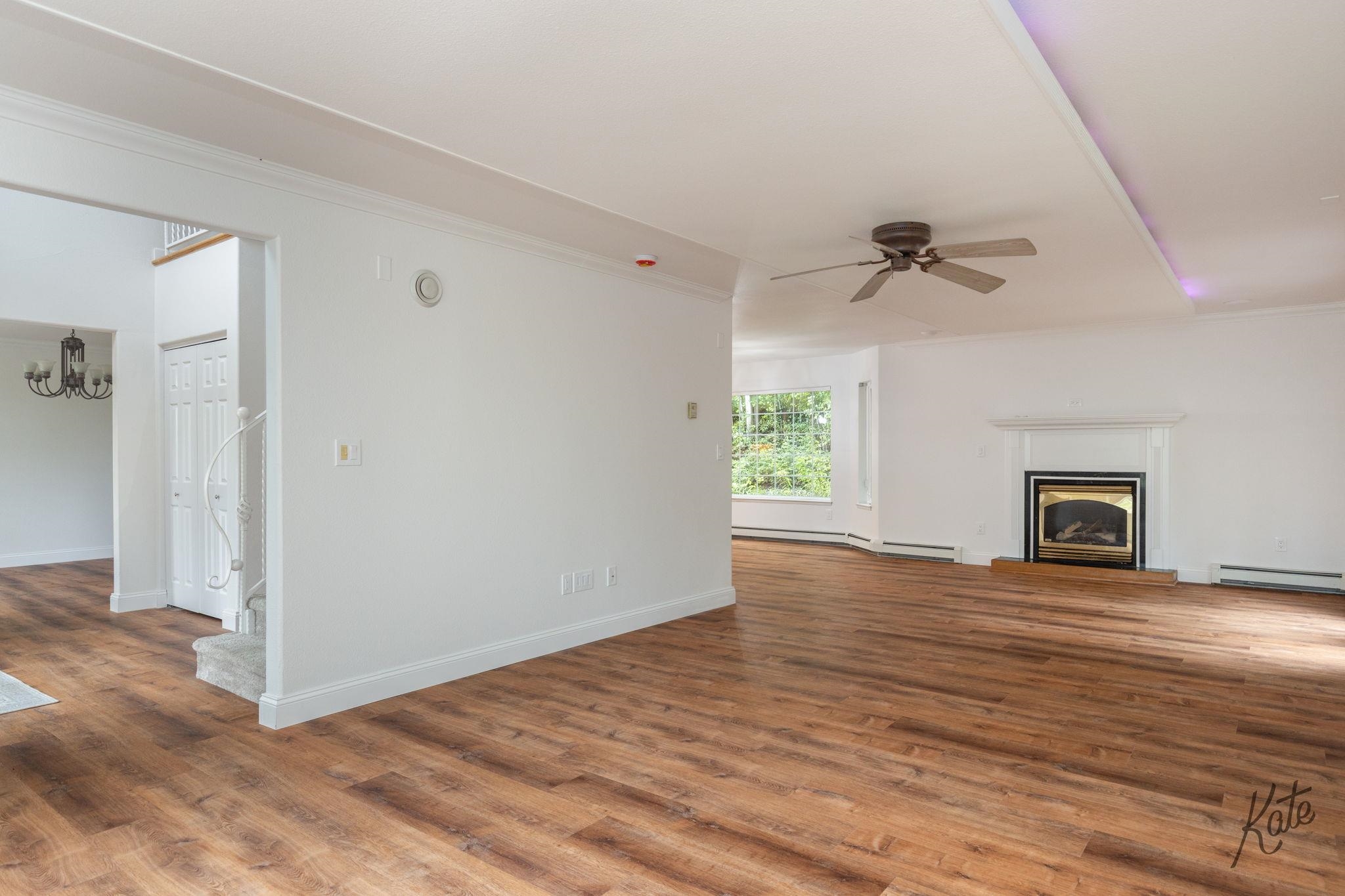 Empty living room with wood-look floors, a white-mantel fireplace, and a large garden-facing window.