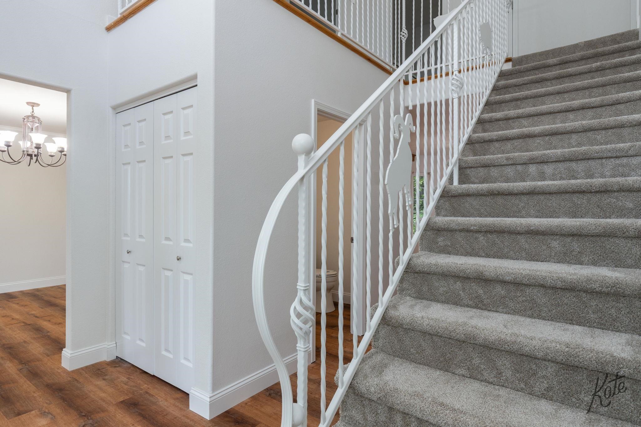 Foyer with a carpeted staircase, ornate white railing, and hardwood flooring.