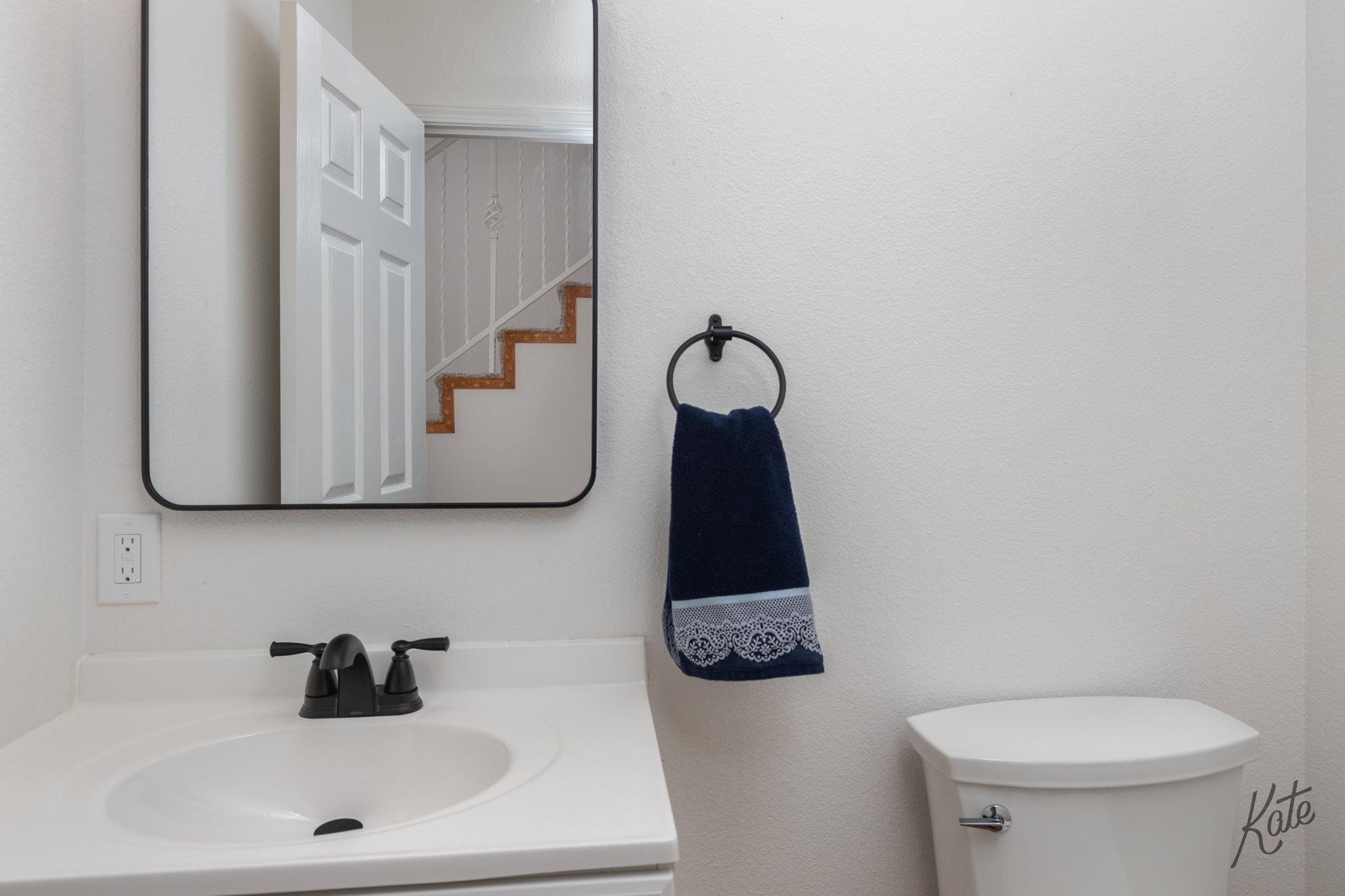 Bathroom vanity with a navy hand towel, toilet, and mirror reflecting the staircase.