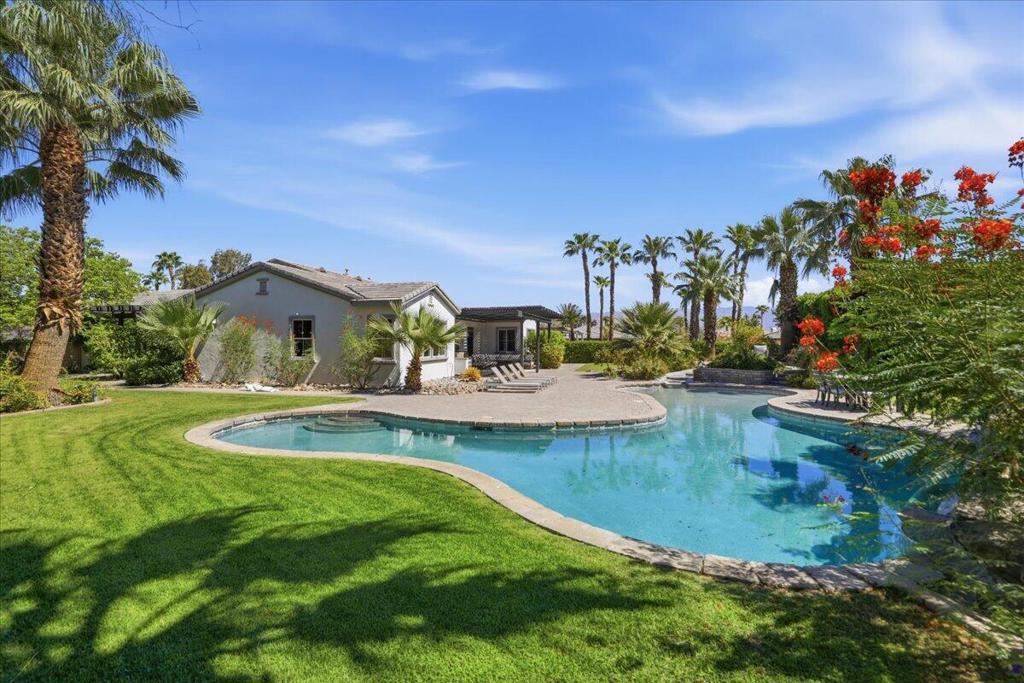 Vacation home beside a curved swimming pool, with a palm-lined lawn and flowering shrubs.