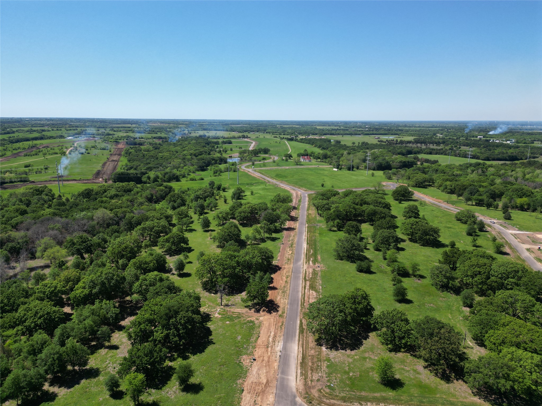 Aerial view of green, tree-dotted land crossed by newly paved winding roads.