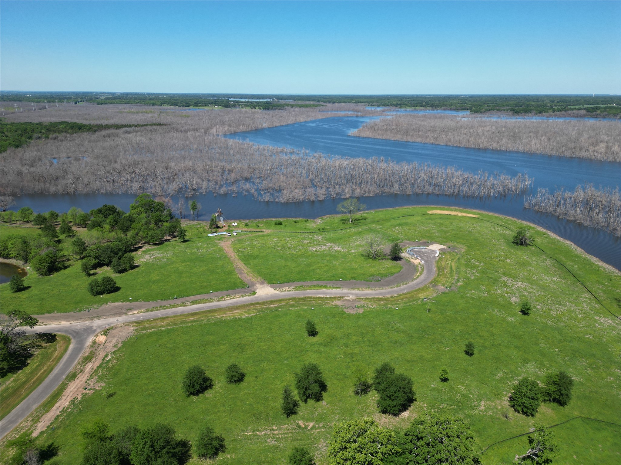Aerial property beside a lake, with a curving road and cleared area near the shoreline.