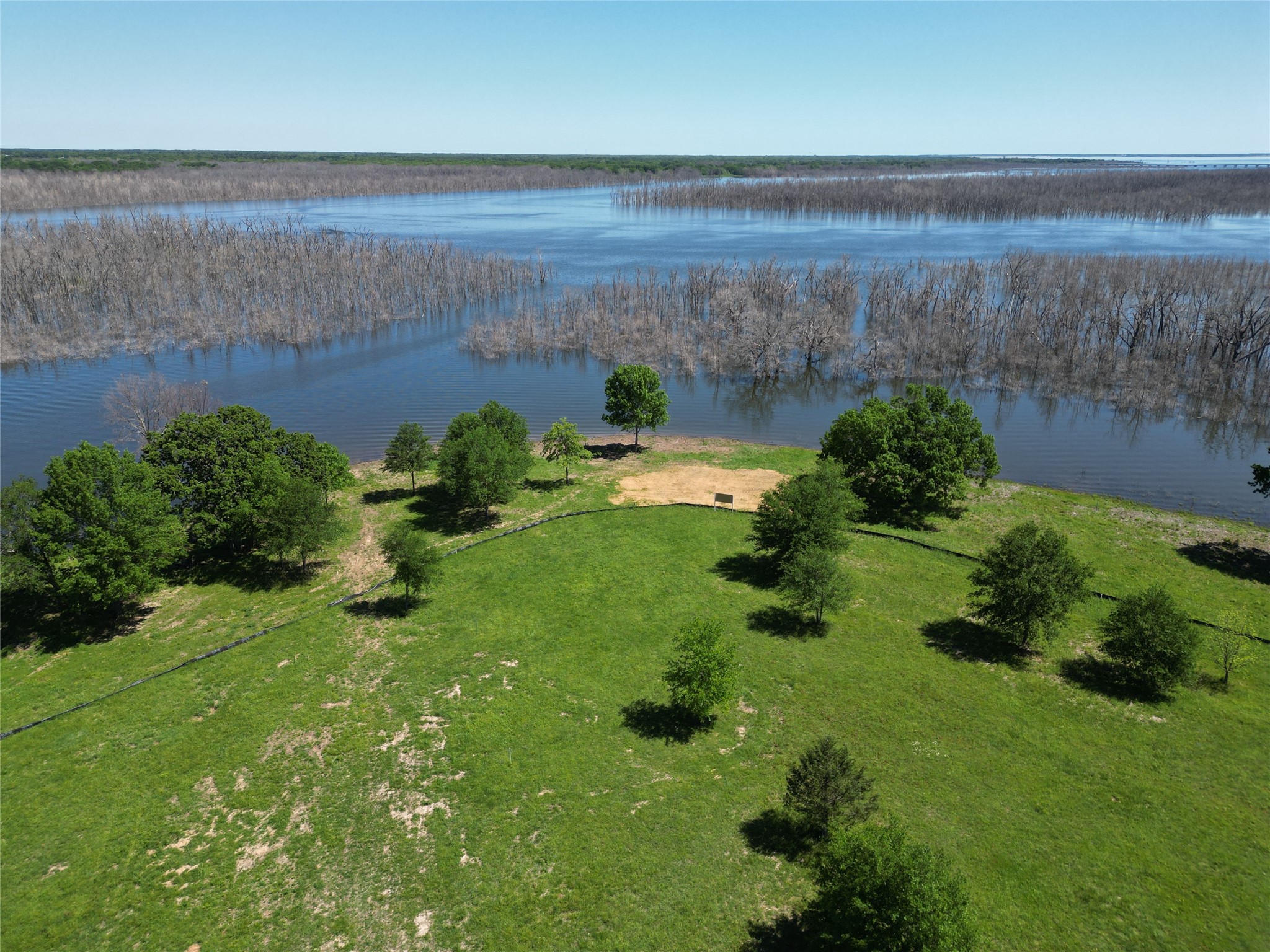 Aerial view of a grassy waterfront property bordered by trees and a broad marsh.