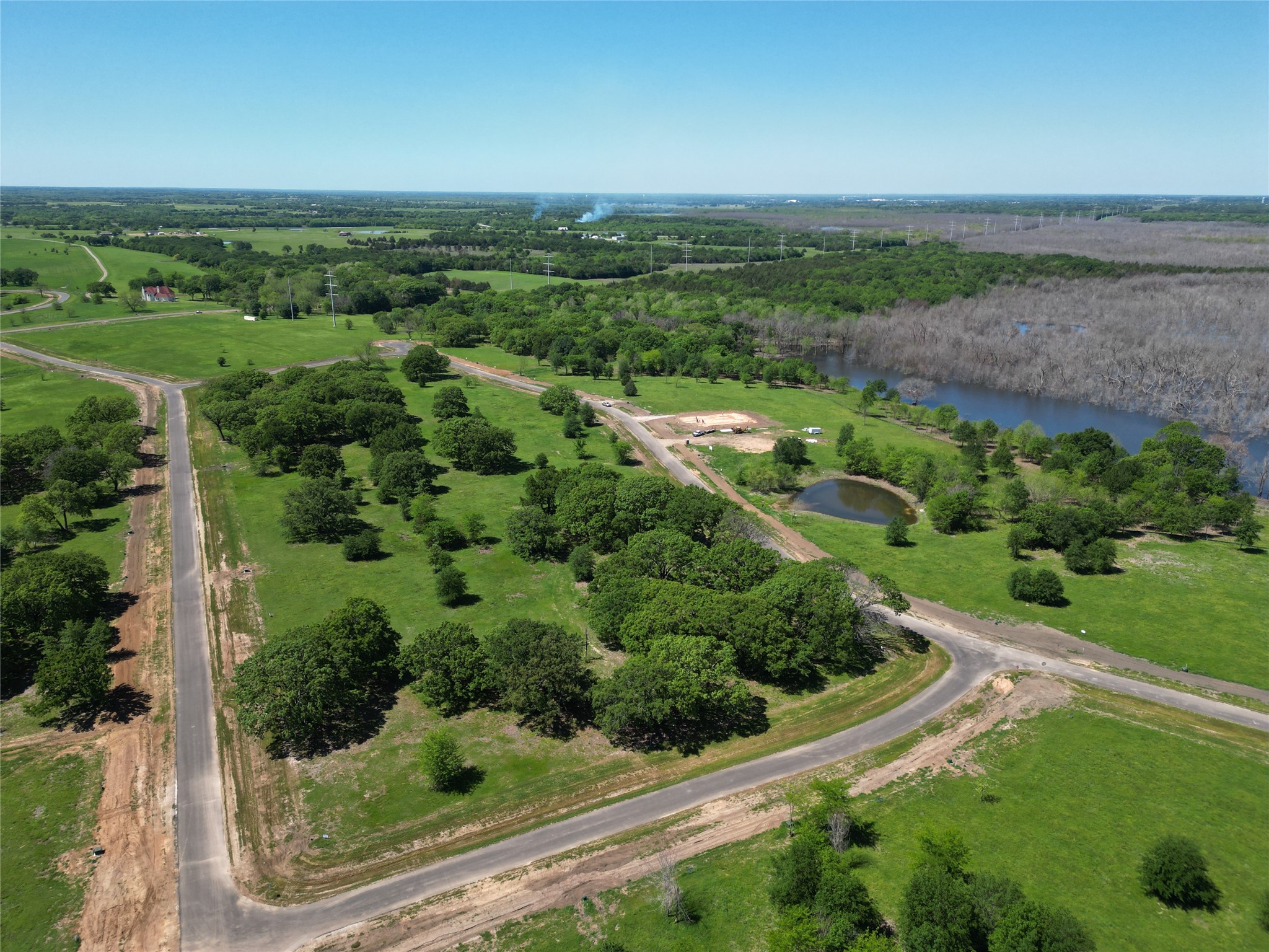 Aerial view of green land with curving roads, a pond, and a wooded shoreline.