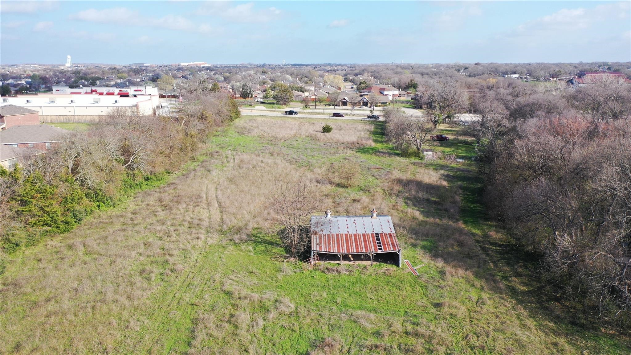 Aerial view of an open grassy property with a weathered metal-roof barn and tree-lined edges.