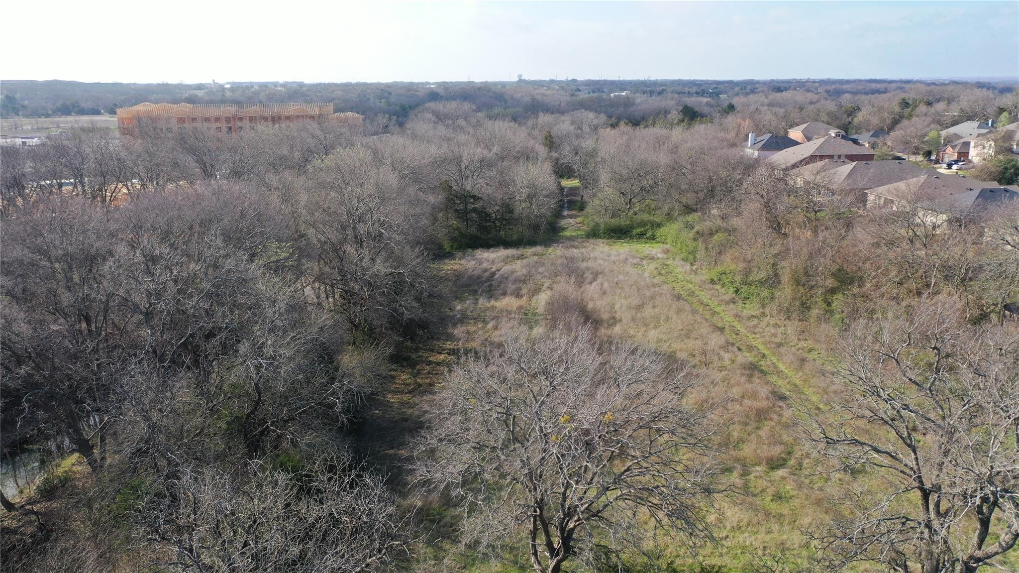 Aerial view of a wooded property with a grassy clearing and neighboring homes.