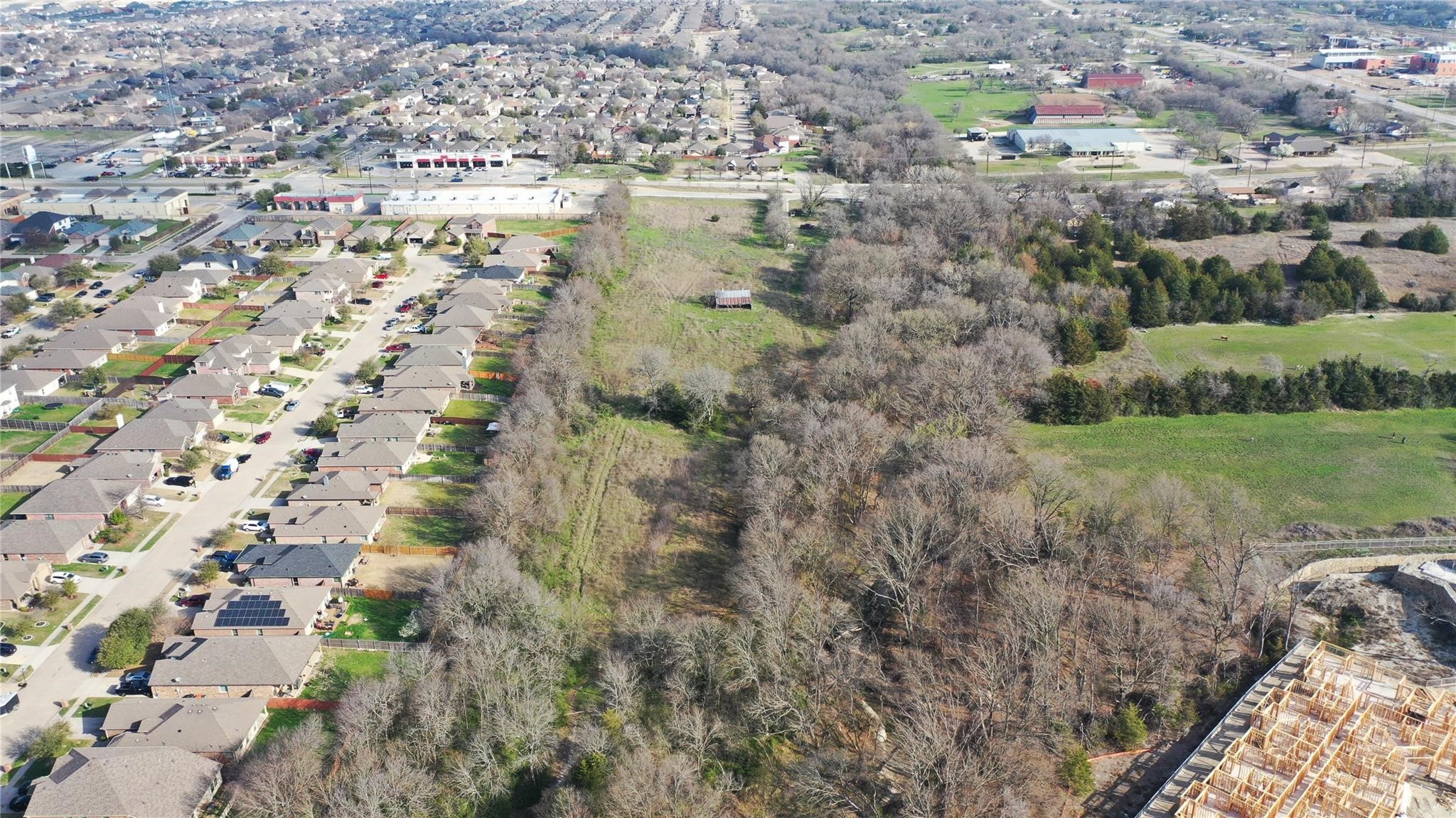Aerial view of wooded land beside a residential neighborhood and open fields.
