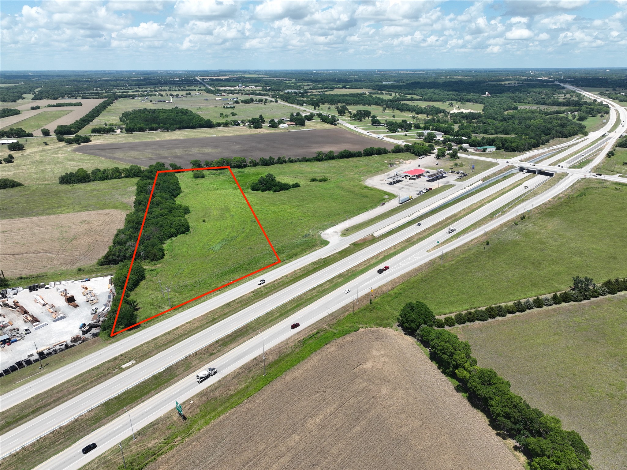 Aerial view of a grassy parcel outlined in red beside a divided highway and interchange.