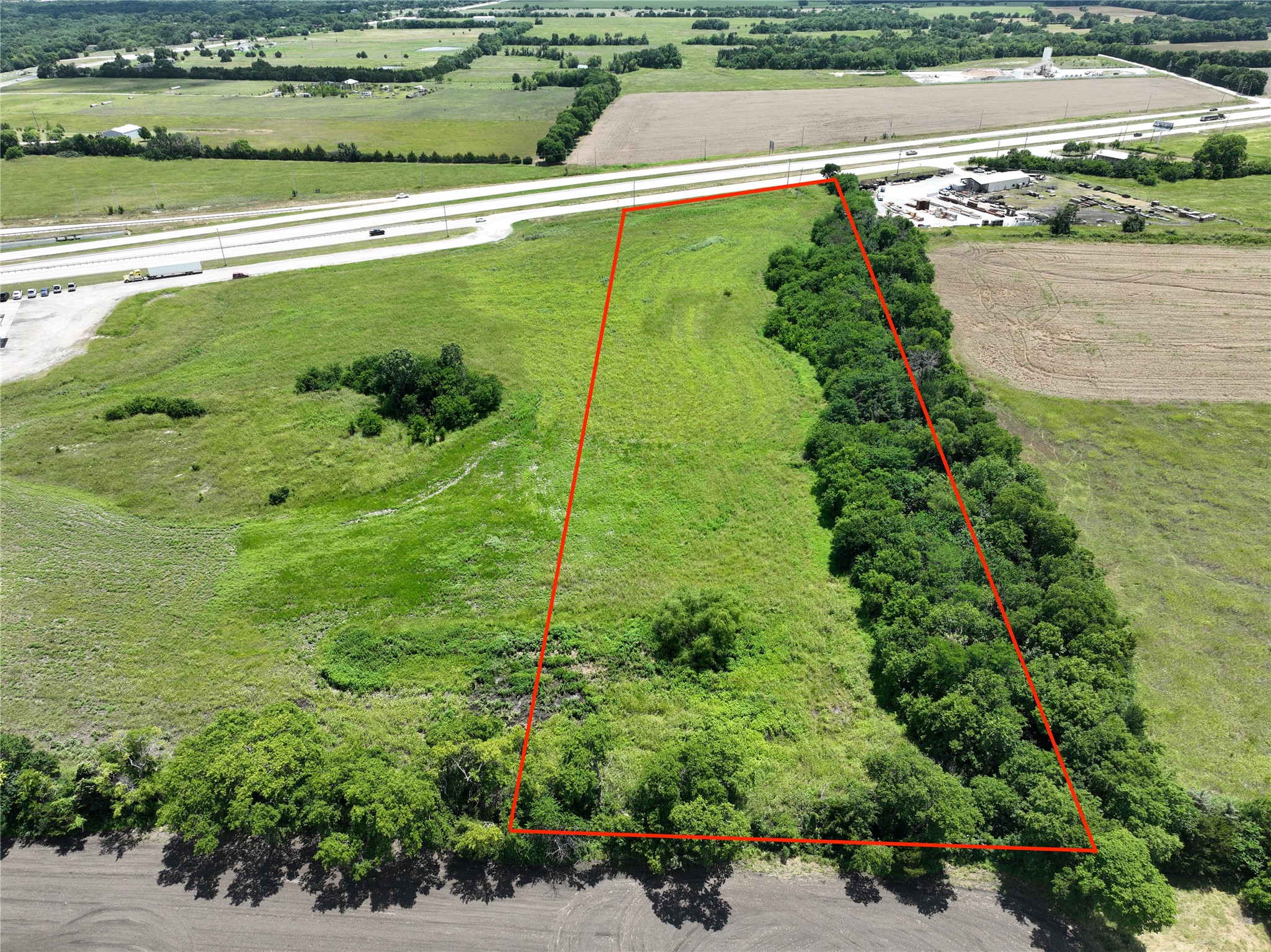 Aerial view of a grassy parcel outlined in red beside Highway 121, bordered by trees.