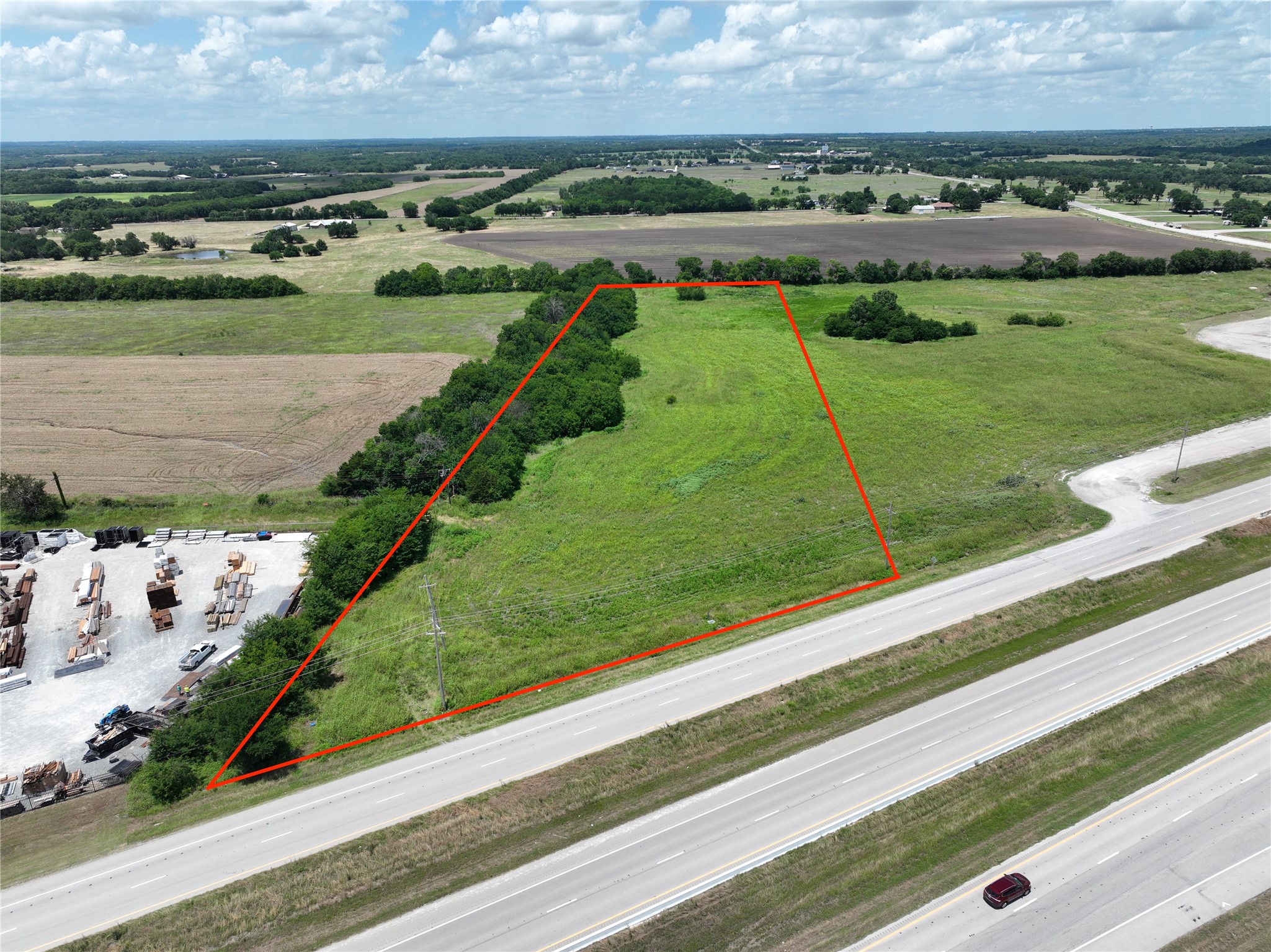 Vacant grassy parcel outlined in red along a divided highway, viewed from above.