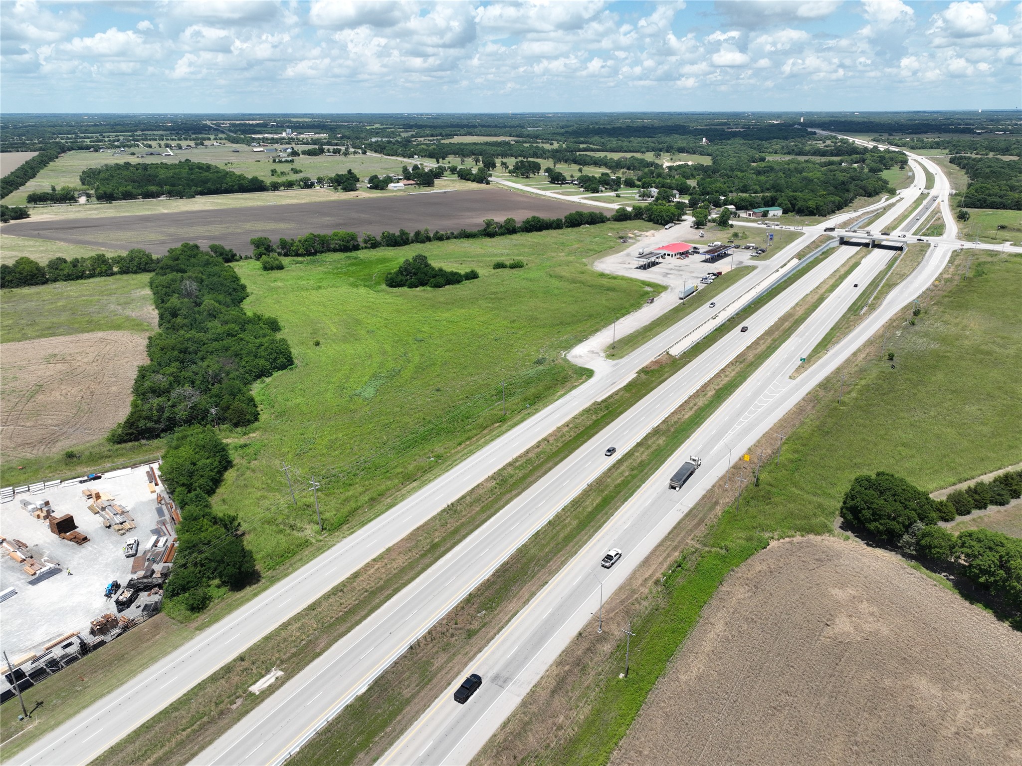 Open green acreage beside a highway interchange, with fields and scattered trees.