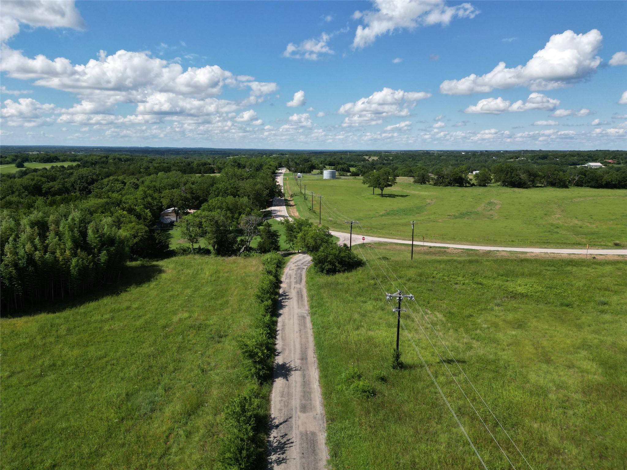 Aerial view of green rural acreage with a gravel driveway, pasture, and tree cover.