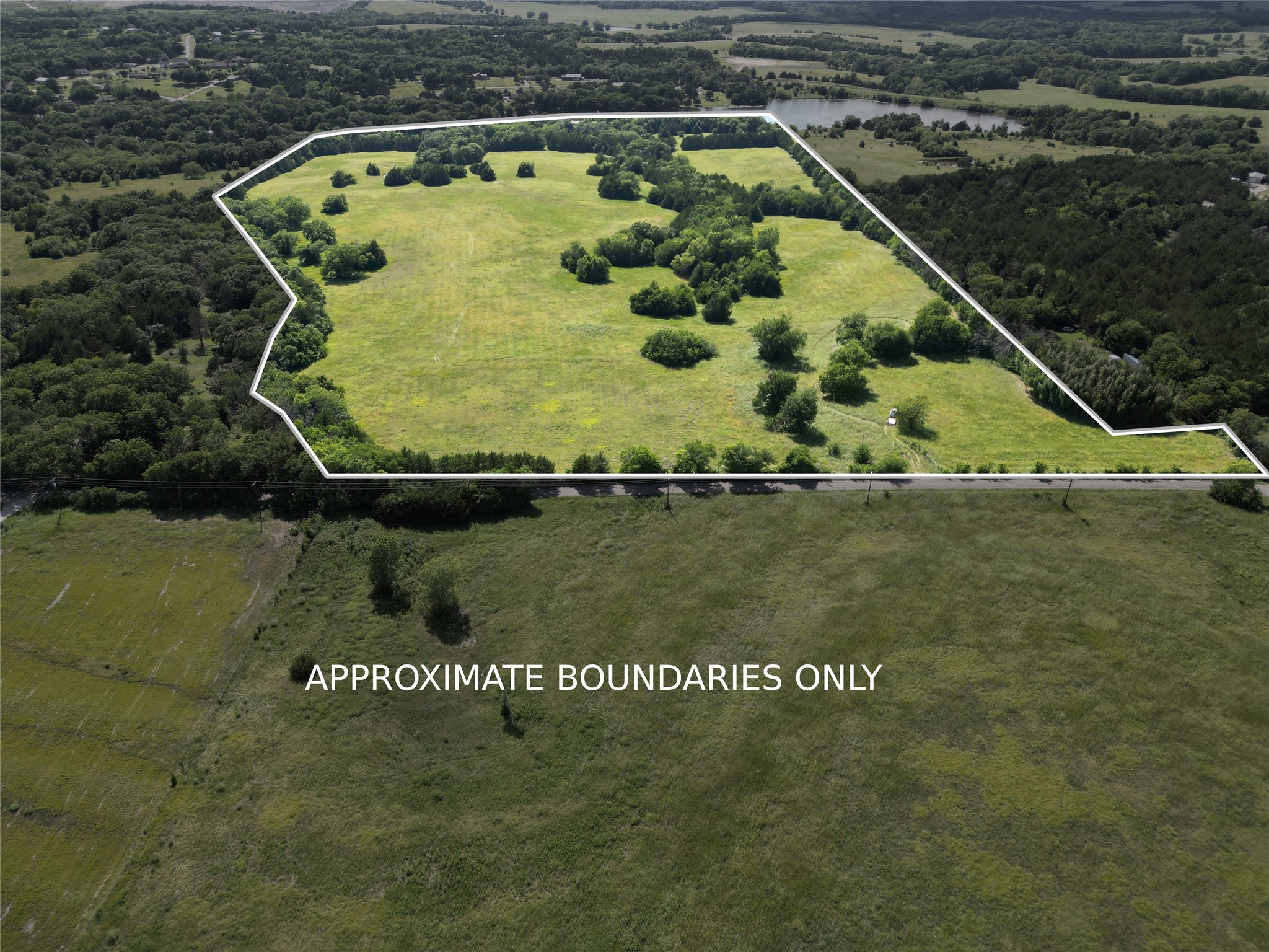 Aerial view of a grassy property with scattered trees and its approximate boundaries outlined in white.