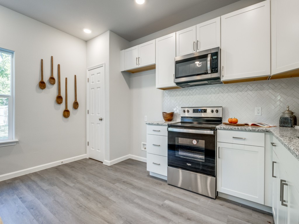 Kitchen with white cabinets, herringbone backsplash, stainless steel appliances, and wooden spoons on the wall.