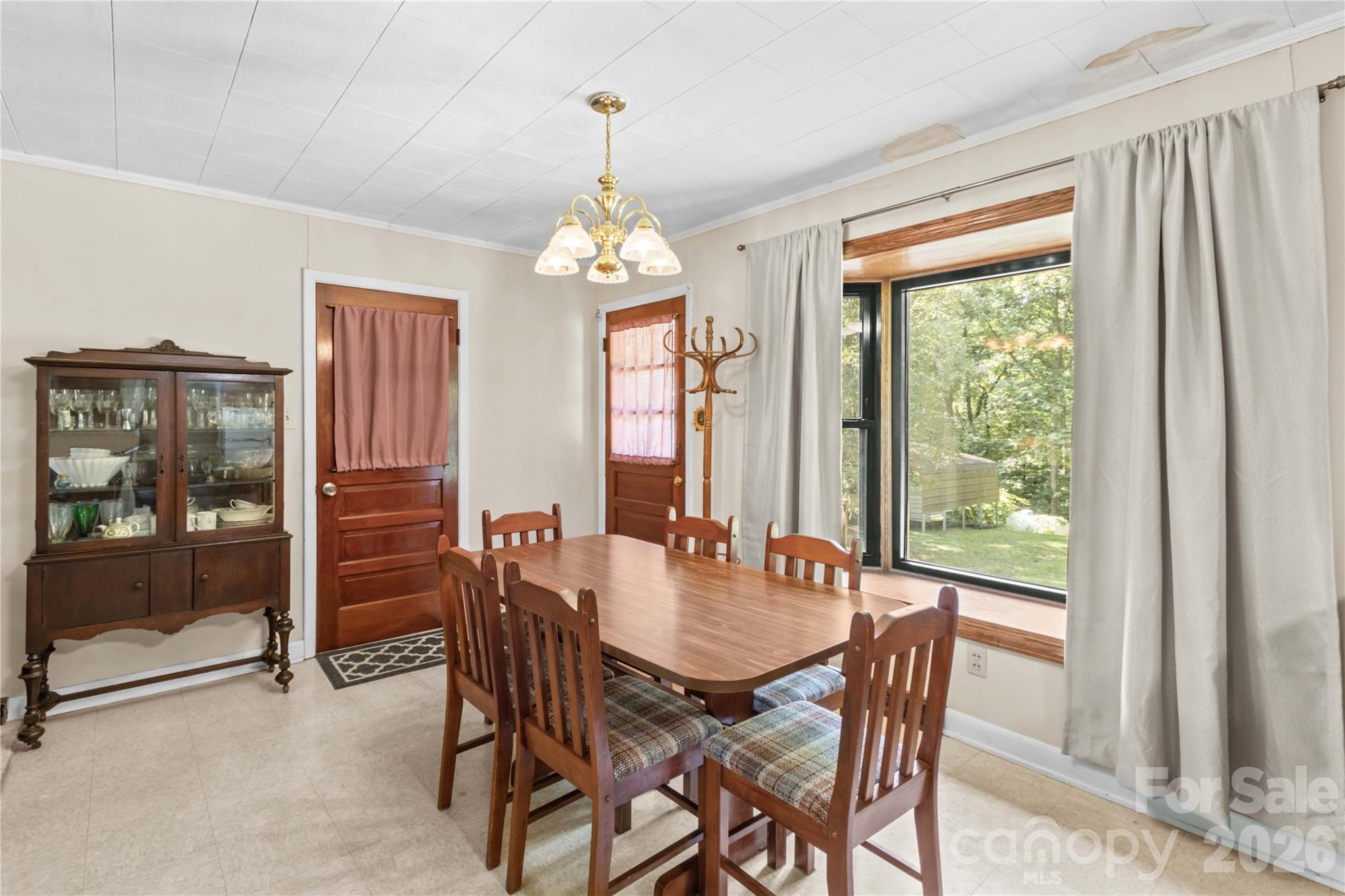 Dining room with a wooden table, glass-front china cabinet, and large windows overlooking trees.