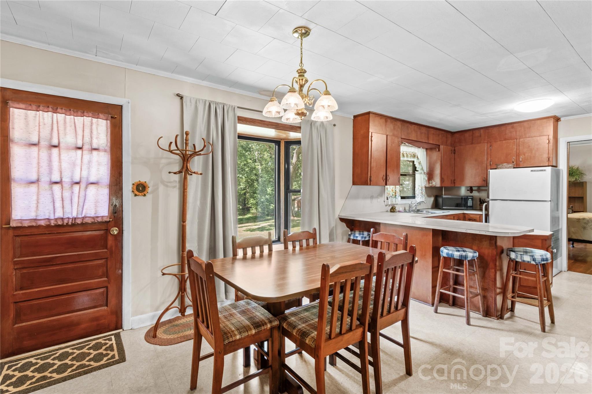 Dining area with a wooden table beside a kitchen with reddish wood cabinets and a breakfast bar.