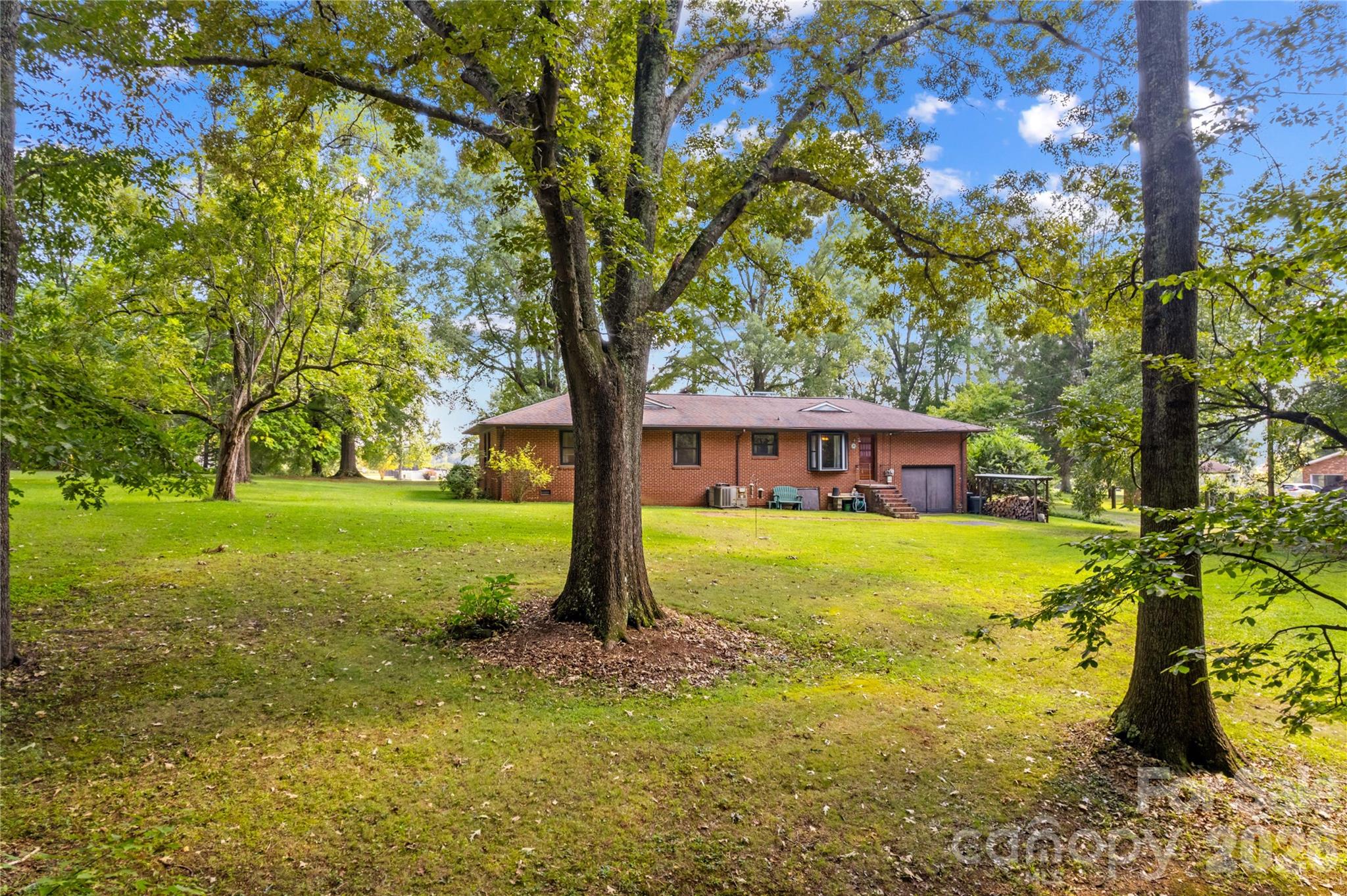 Brick ranch home and garage beyond a spacious lawn shaded by mature trees.