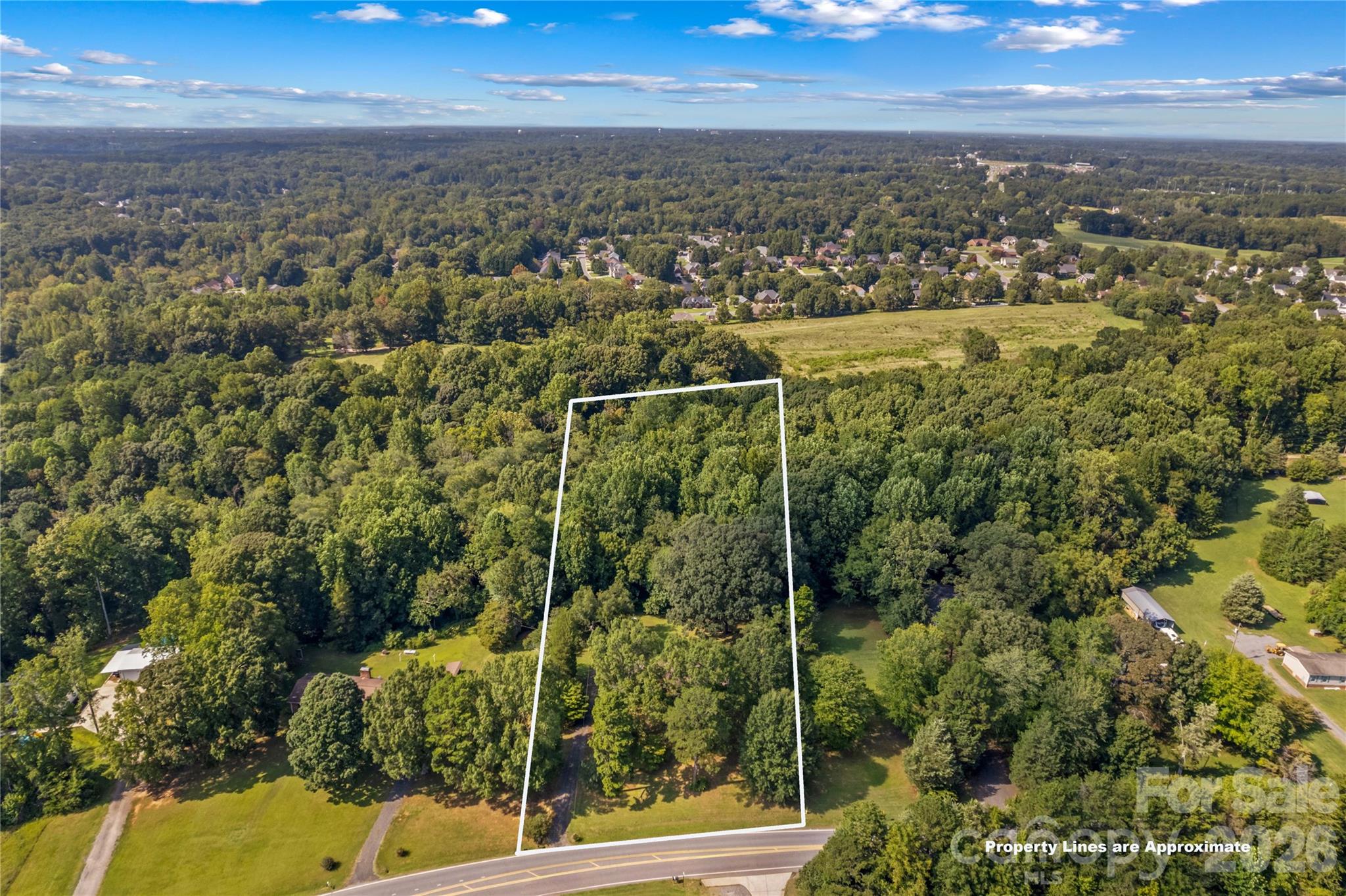 Aerial view of a wooded lot outlined beside a road, with homes and forest nearby.