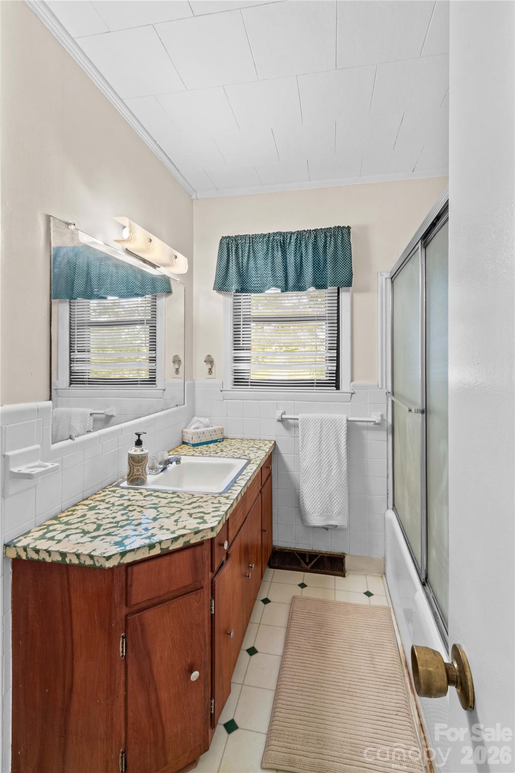 Bathroom with a long wooden vanity, patterned countertop, and sliding glass shower door.