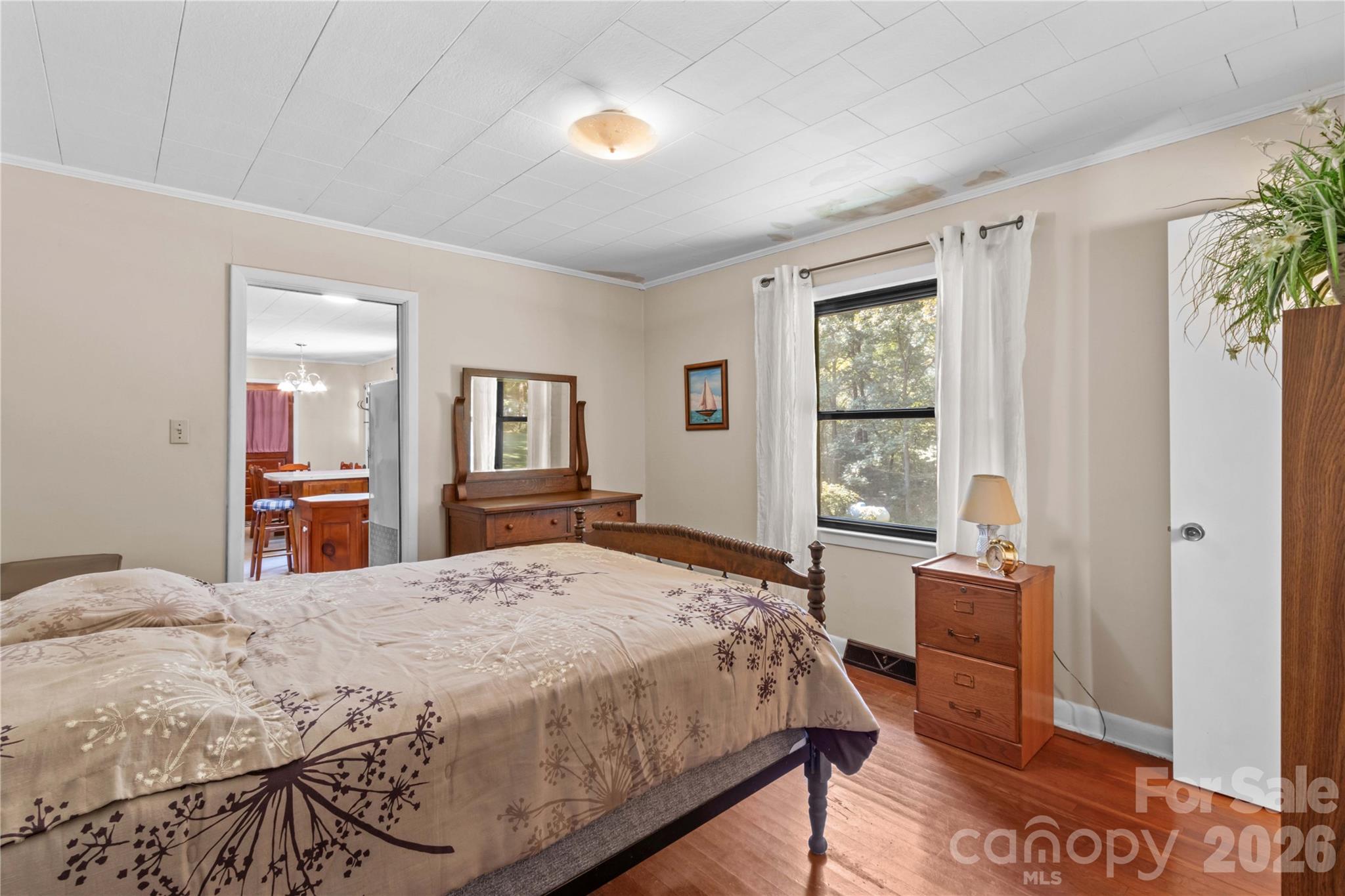 Furnished bedroom with a wooden bed and matching furniture, hardwood floors, and a curtained window.