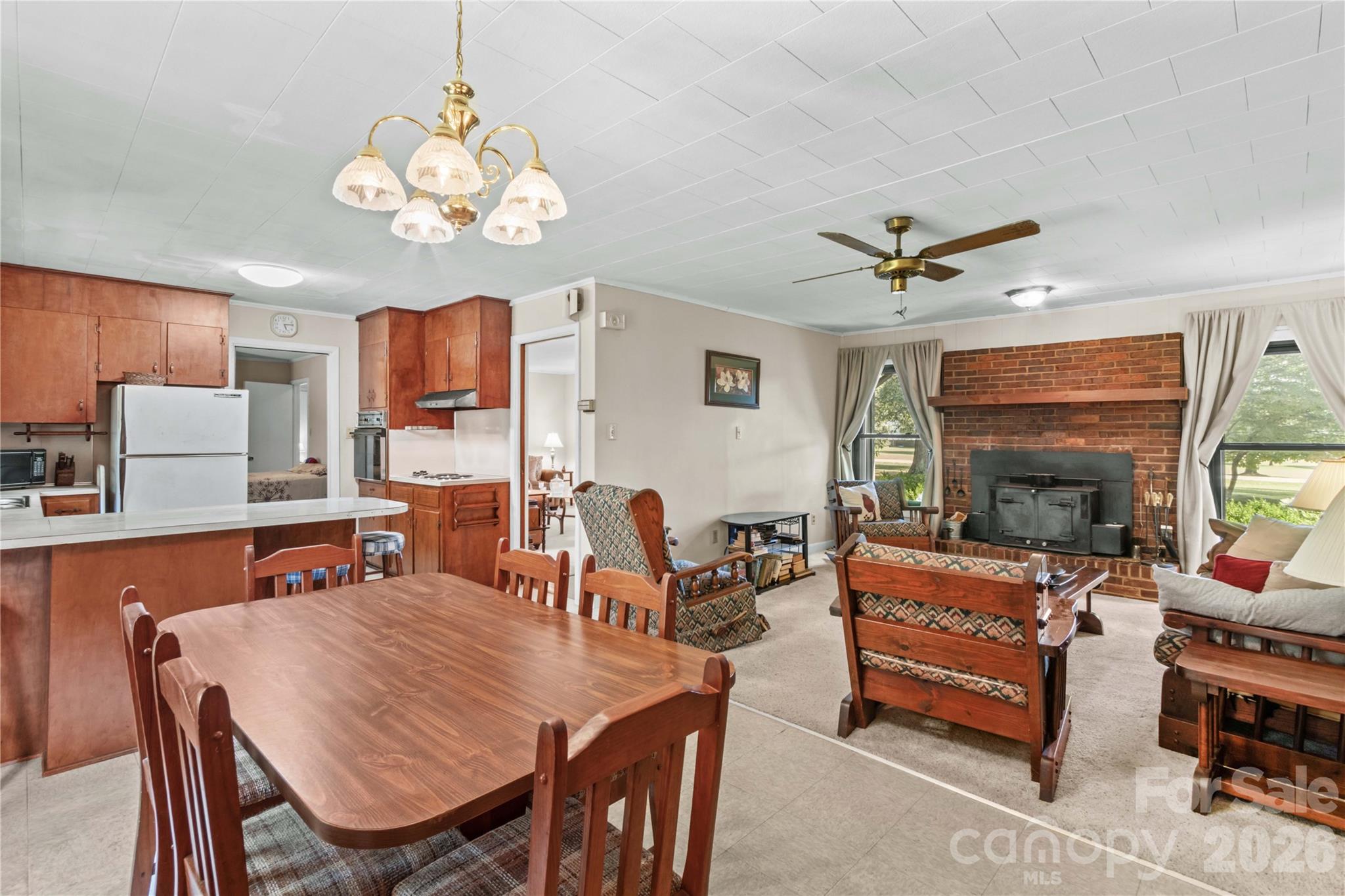 Open kitchen, dining, and living room with wood cabinets and a brick fireplace.