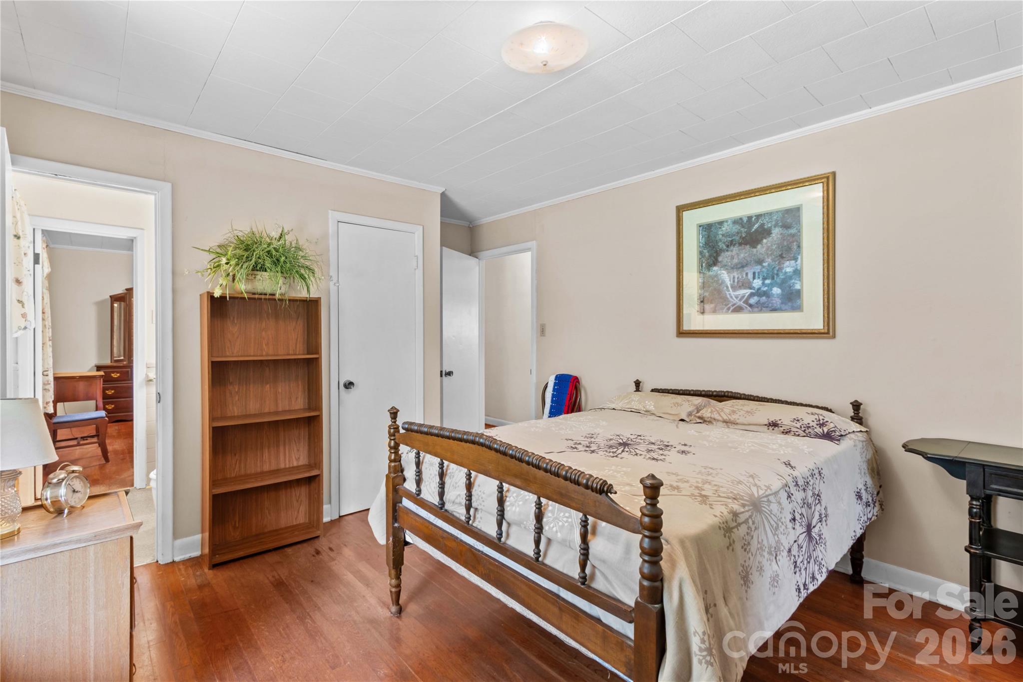 Furnished bedroom with carved wooden bed, patterned bedding, and a plant-topped bookcase.