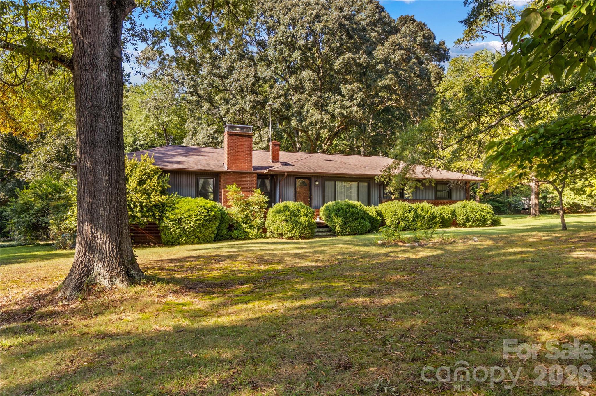 Single-story home with brick chimneys and a covered porch, framed by mature trees and a broad lawn.
