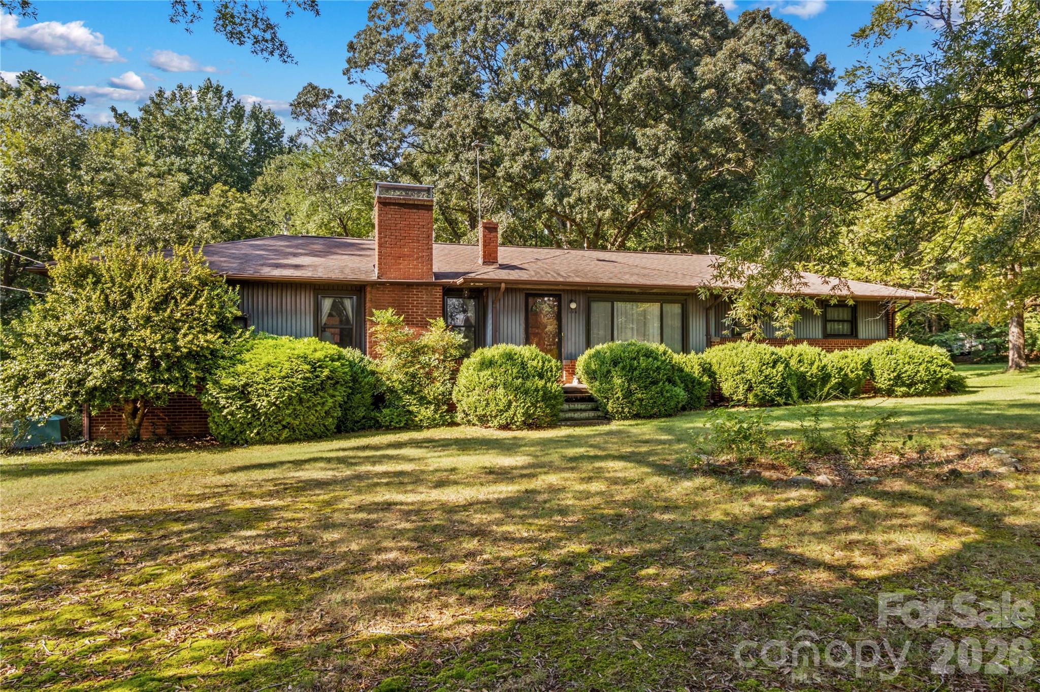 Single-story brick-and-siding home with a broad shaded lawn and mature trees.
