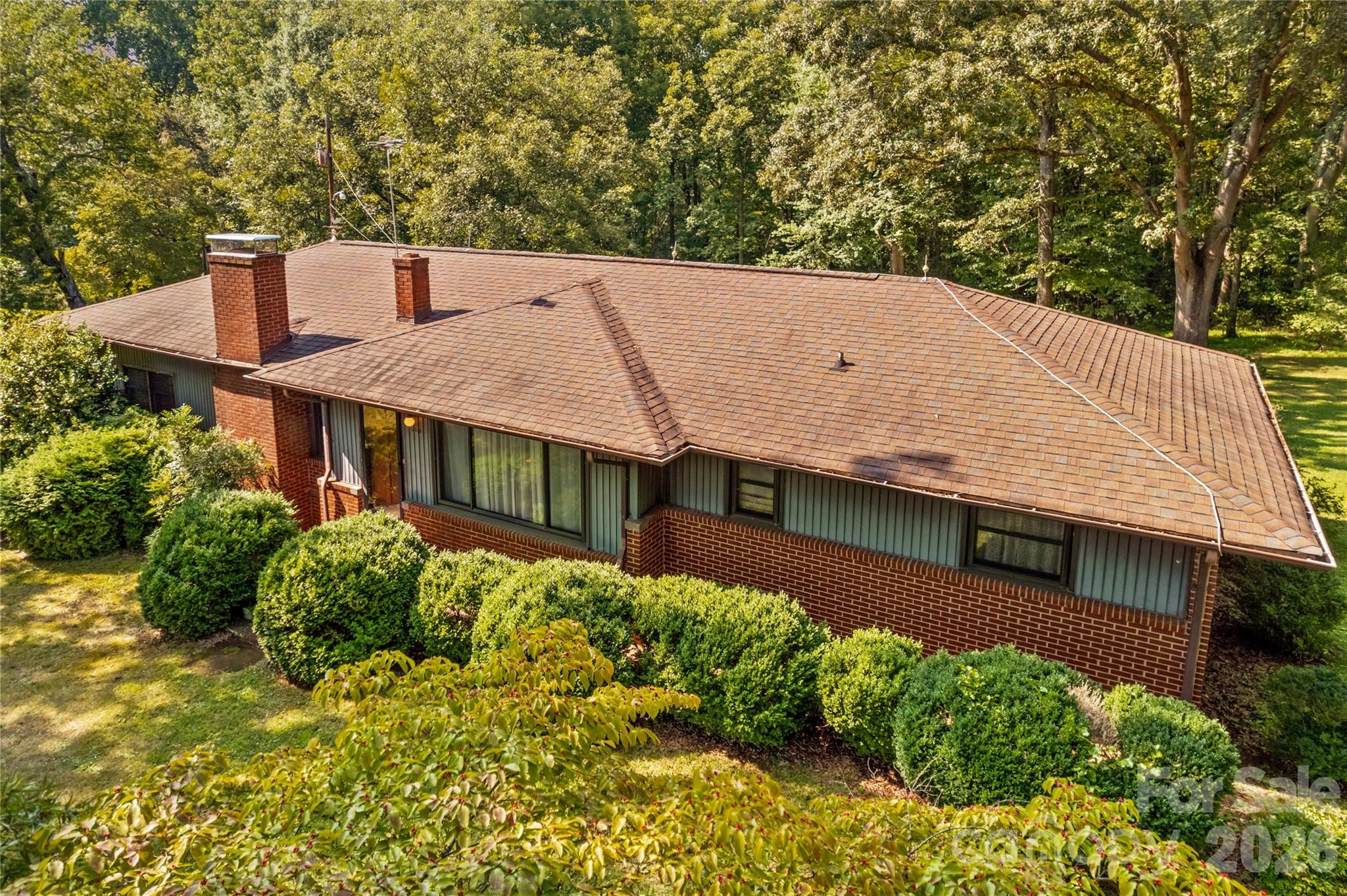Aerial view of a single-story brick house with two chimneys and a broad shingle roof.
