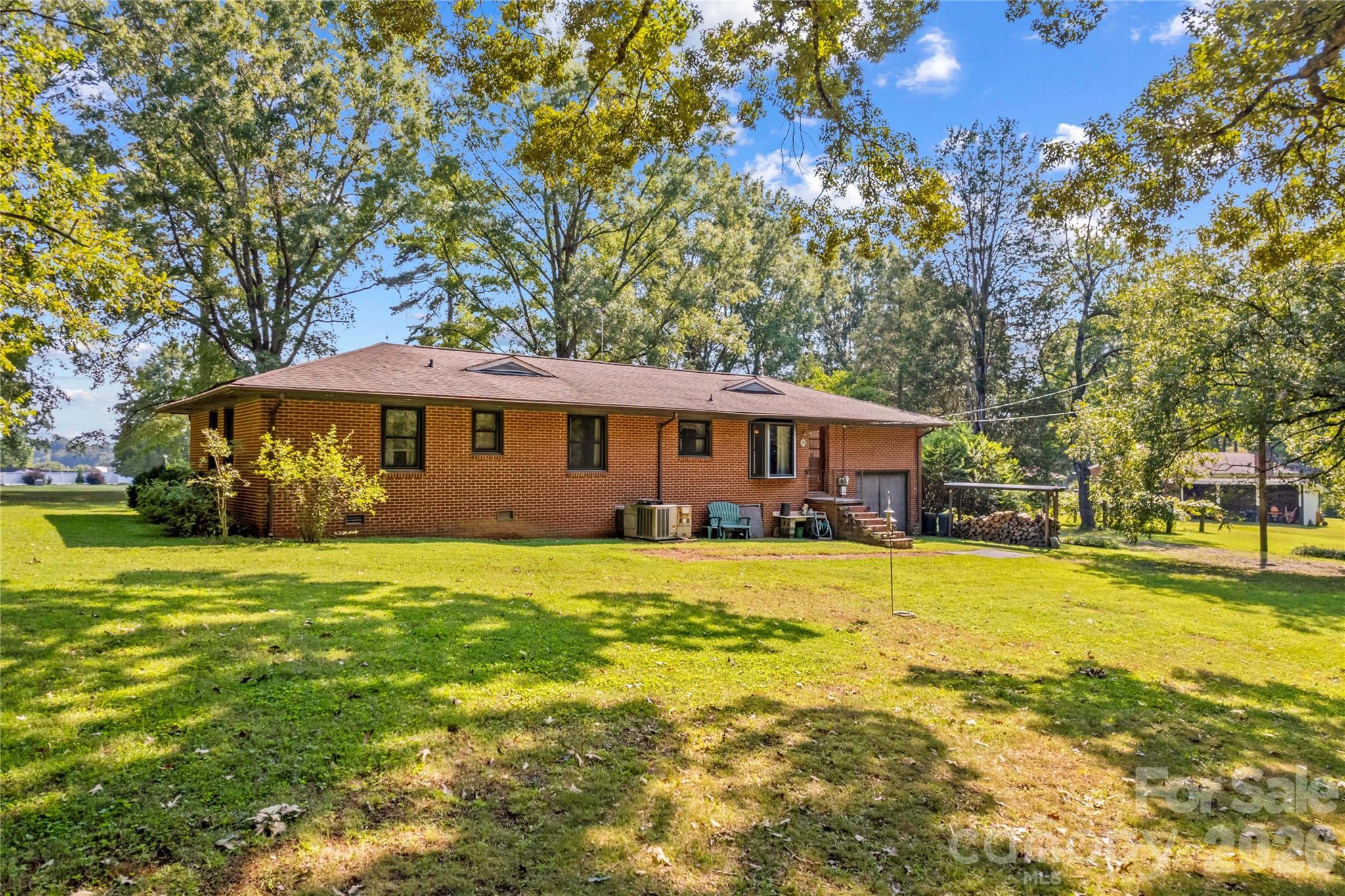 Red brick ranch house beside a broad lawn, shaded by mature trees.
