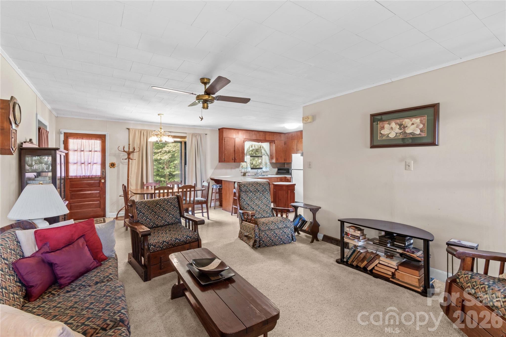 Living room with patterned armchairs and a view into the dining area and wood-cabinet kitchen.