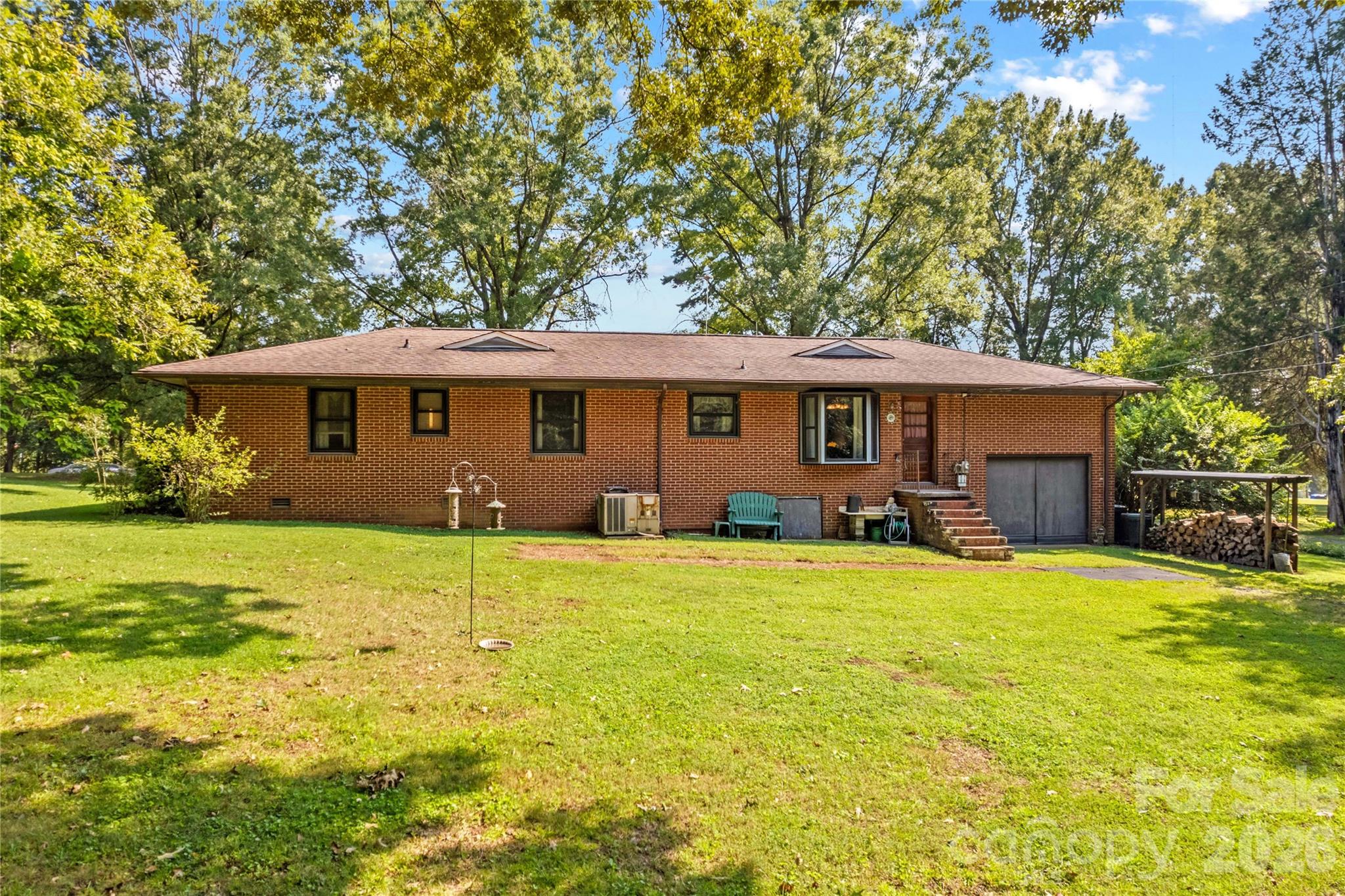 Red brick house with a garage and broad grassy yard beneath mature trees.