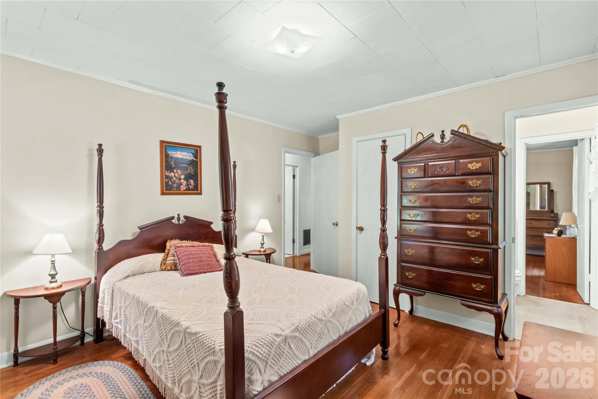 Bedroom with a dark wood four-poster bed and tall matching dresser on hardwood floors.