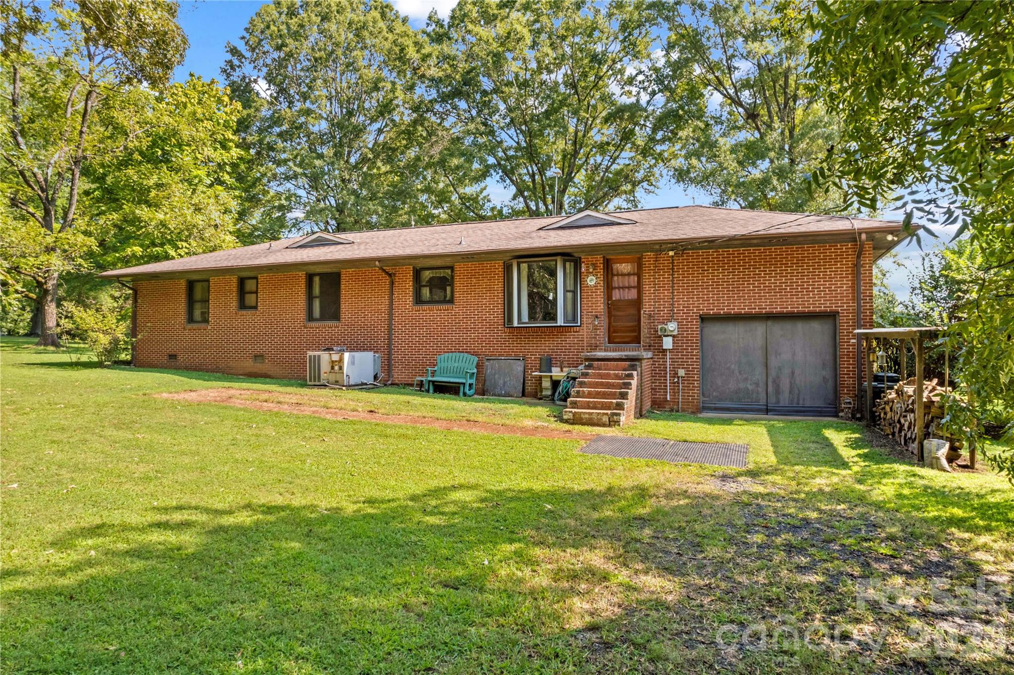 Single-story brick house with an attached garage, brick entry steps, and mature trees around a broad lawn.