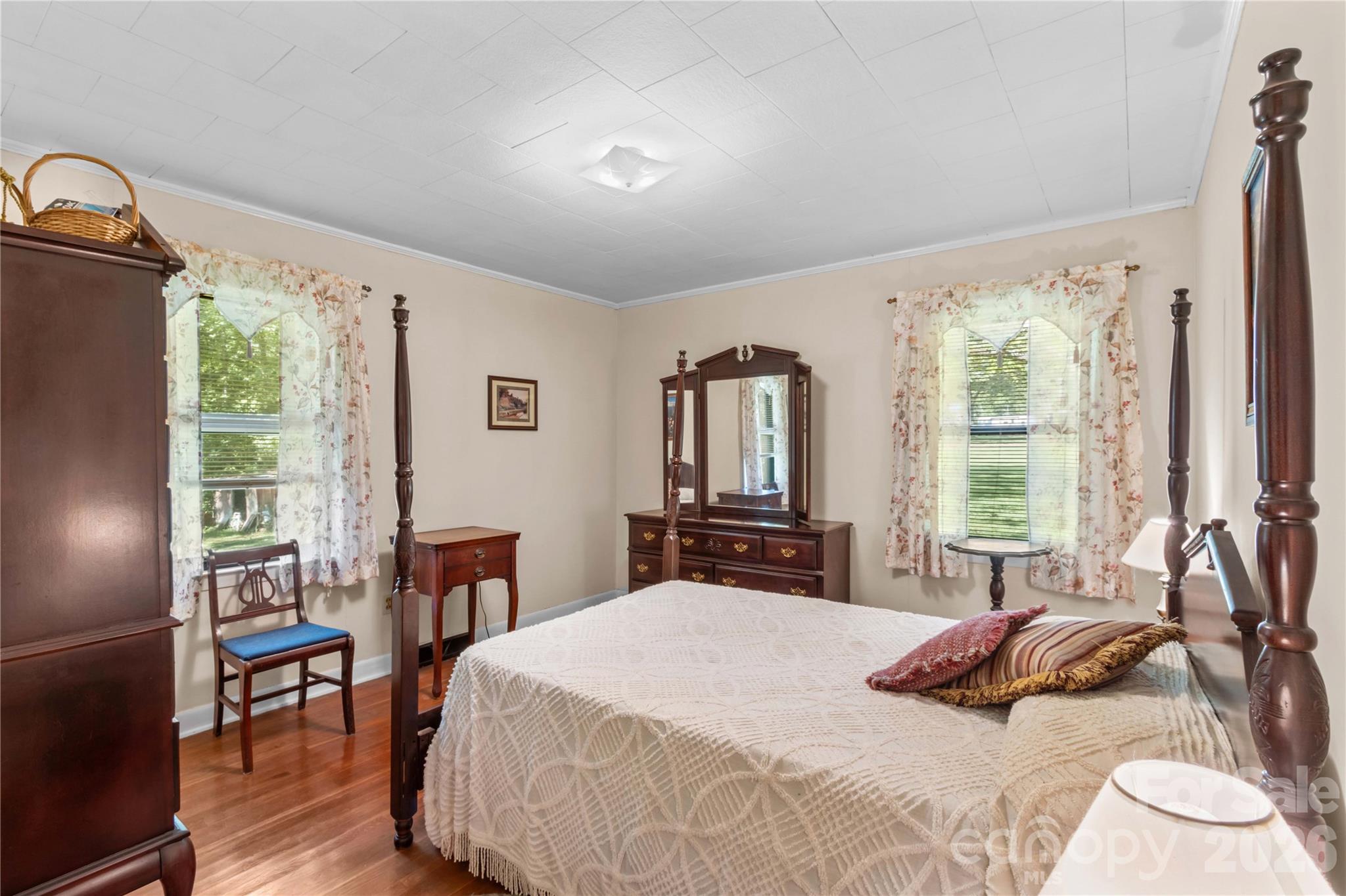 Bedroom with a dark wood four-poster bed, matching dresser, and floral curtains.
